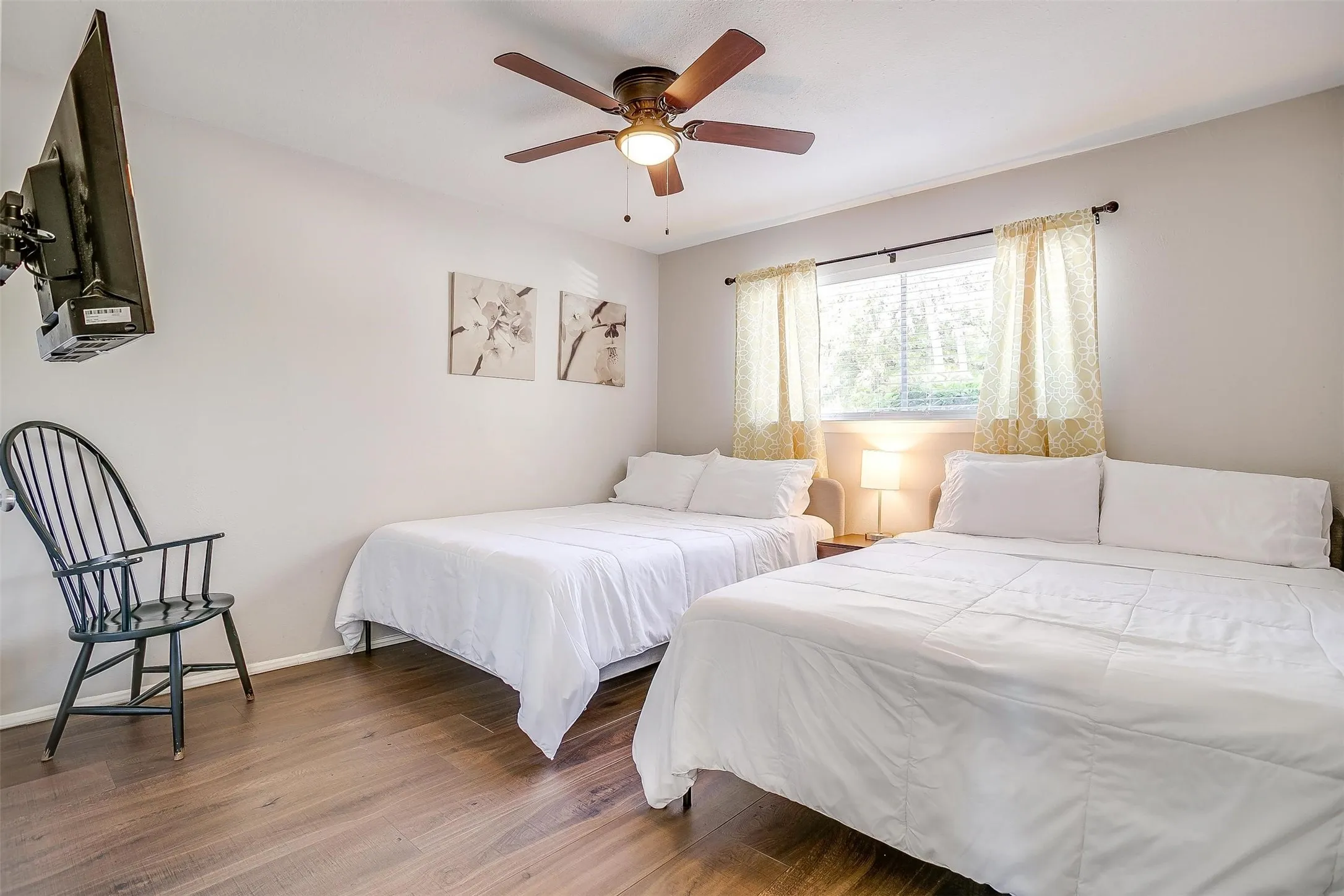 Bedroom featuring wood-finish flooring, a ceiling fan with integrated lighting, and a window with patterned curtains