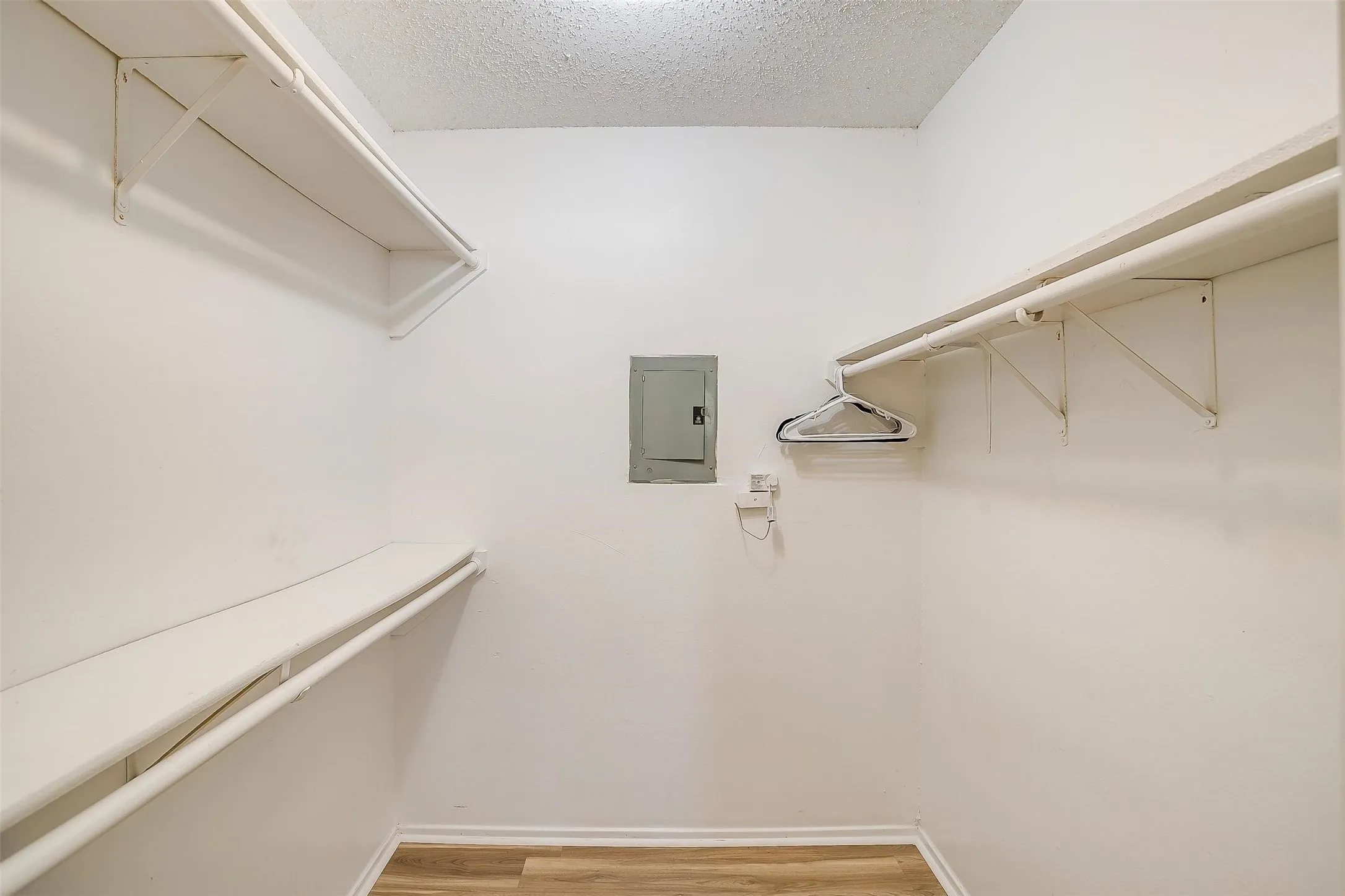 Walk-in closet with multiple white wire shelving units, hanging rods, and wood-finish flooring