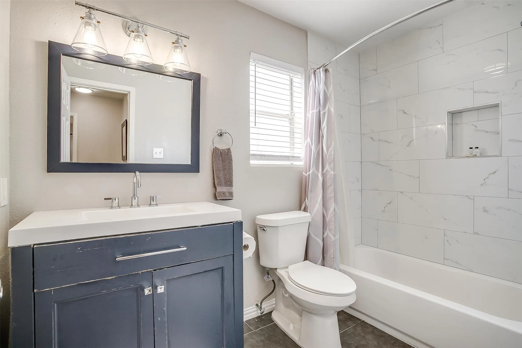 Bathroom featuring a white subway-tiled shower with a built-in niche, a white ceramic bathtub, and a dark blue vanity with a white countertop and rectangular sink