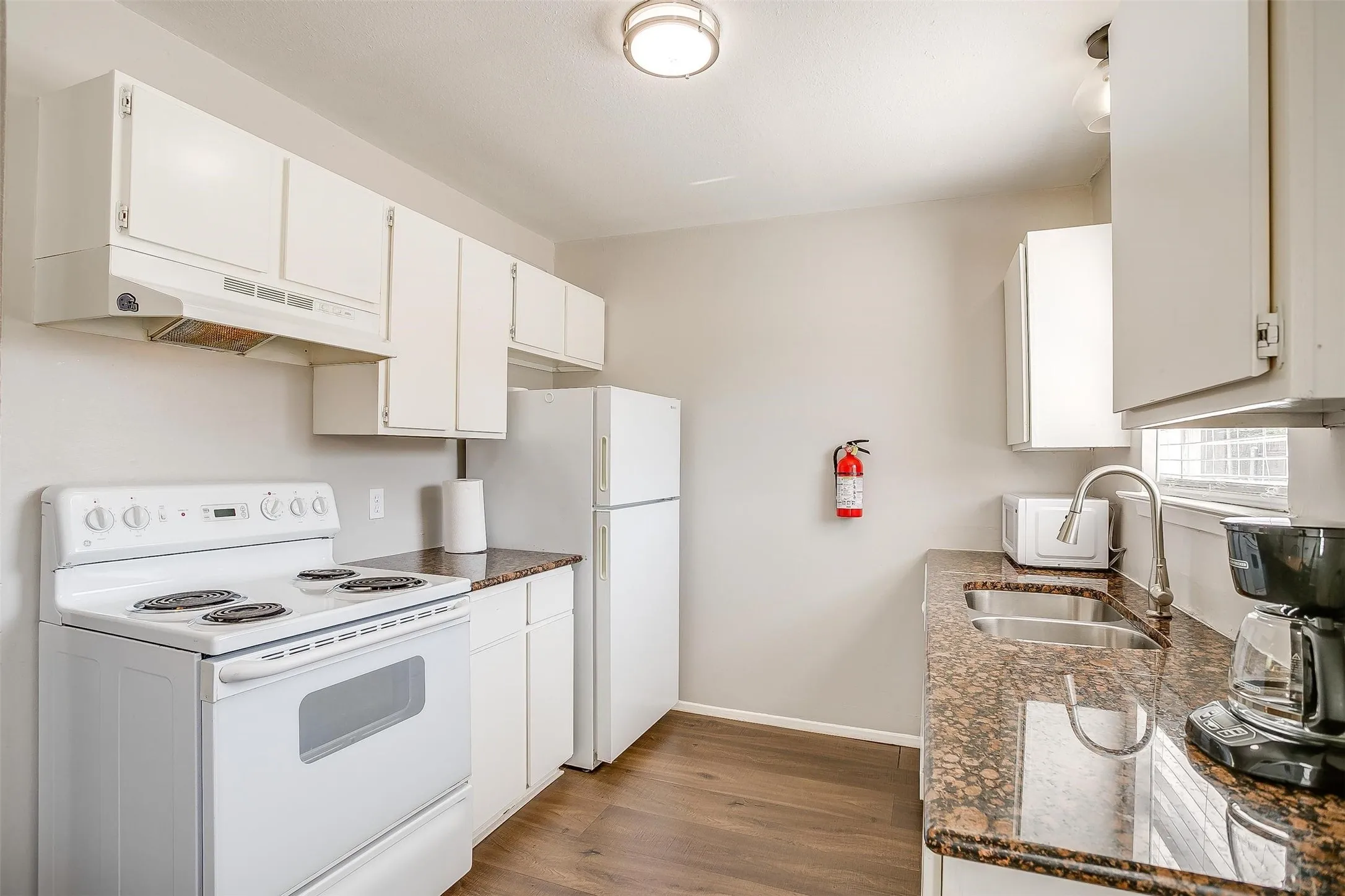 Kitchen featuring white cabinetry, brown granite-finish countertops, and wood-finish flooring