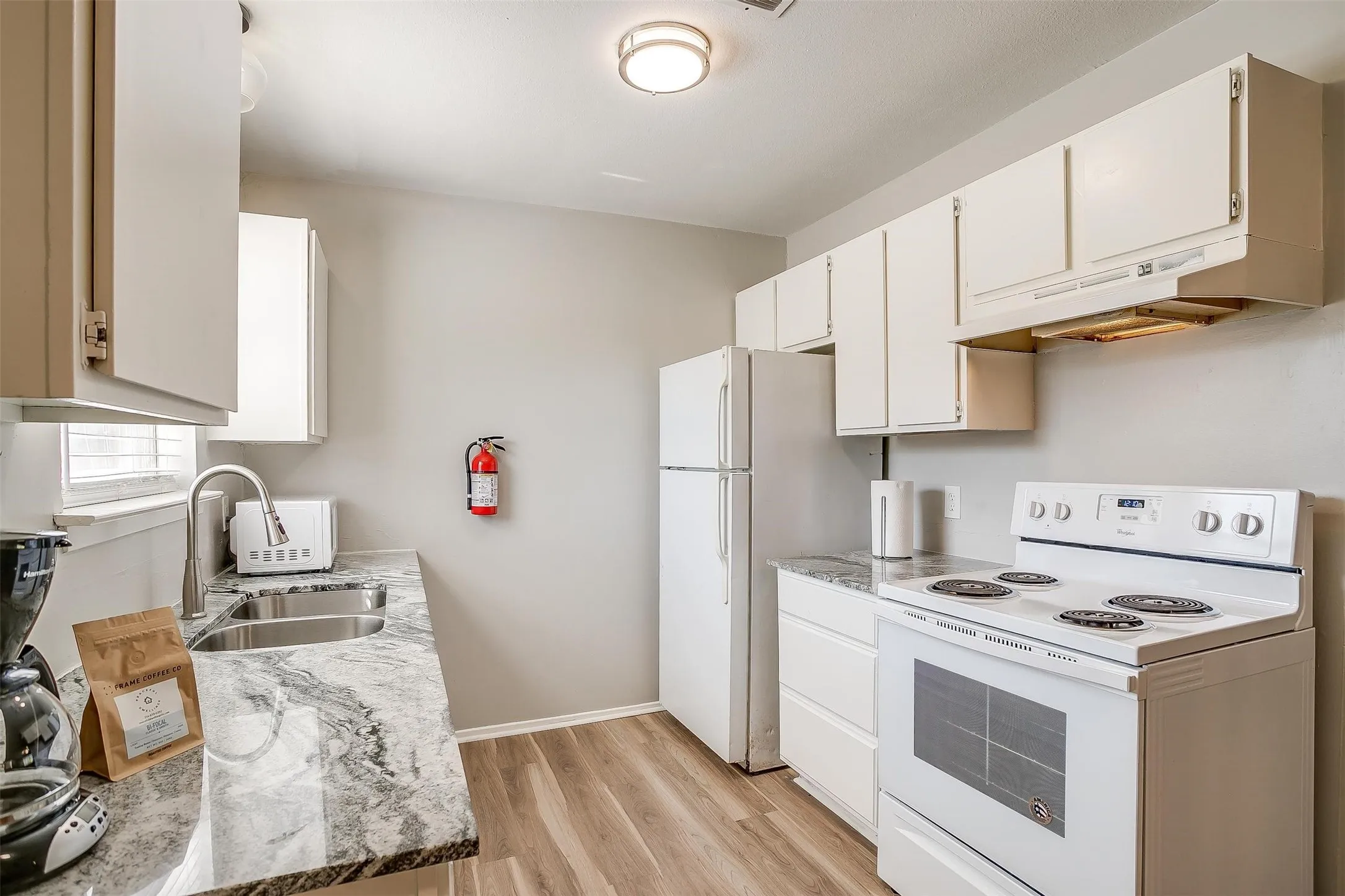 Kitchen featuring white cabinetry, stone-finish countertops, stainless steel sink with gooseneck faucet, white appliances, and wood-finish flooring