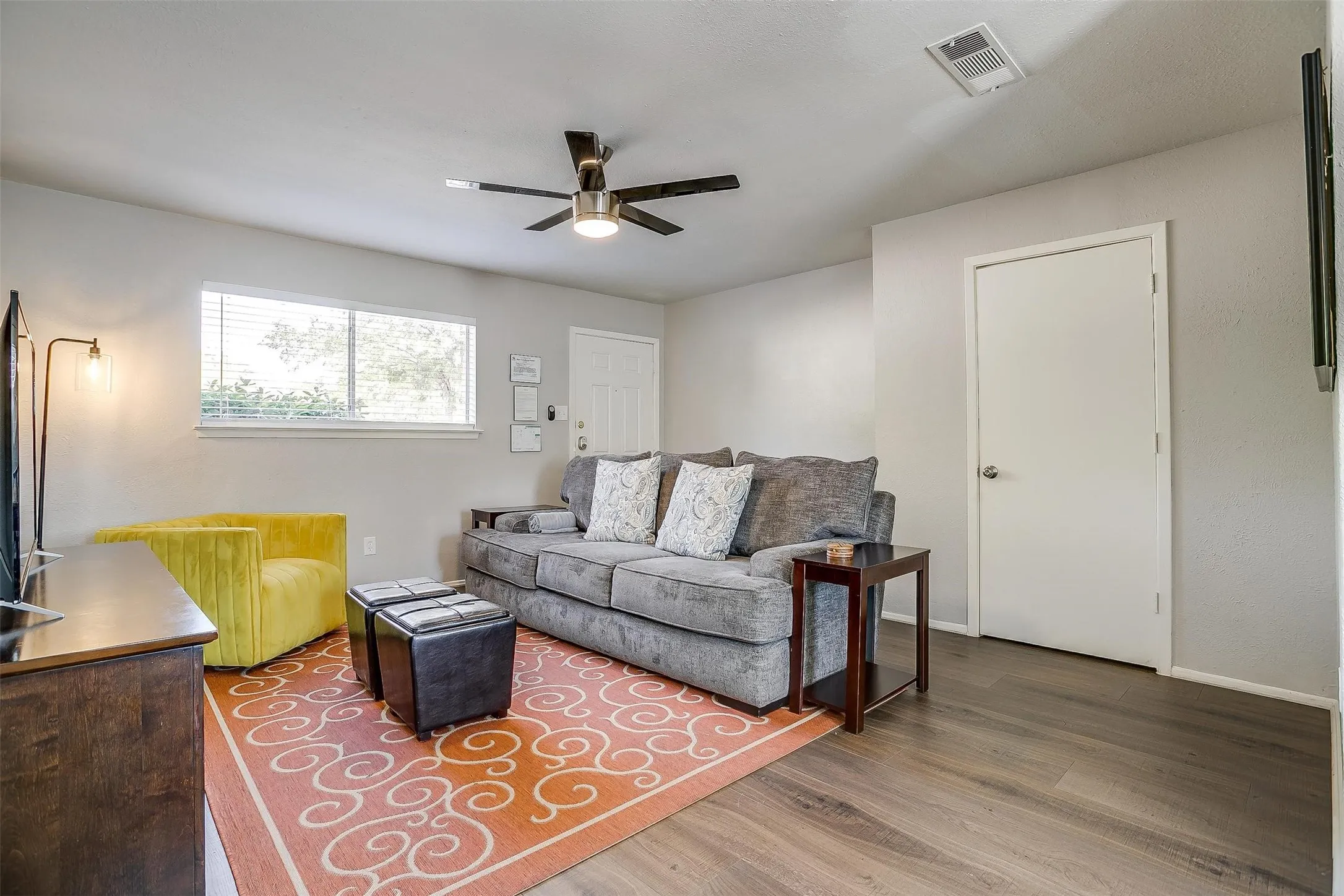 Living area featuring wood-finish flooring, a ceiling fan with integrated lighting, a large window with horizontal blinds, and neutral wall tones