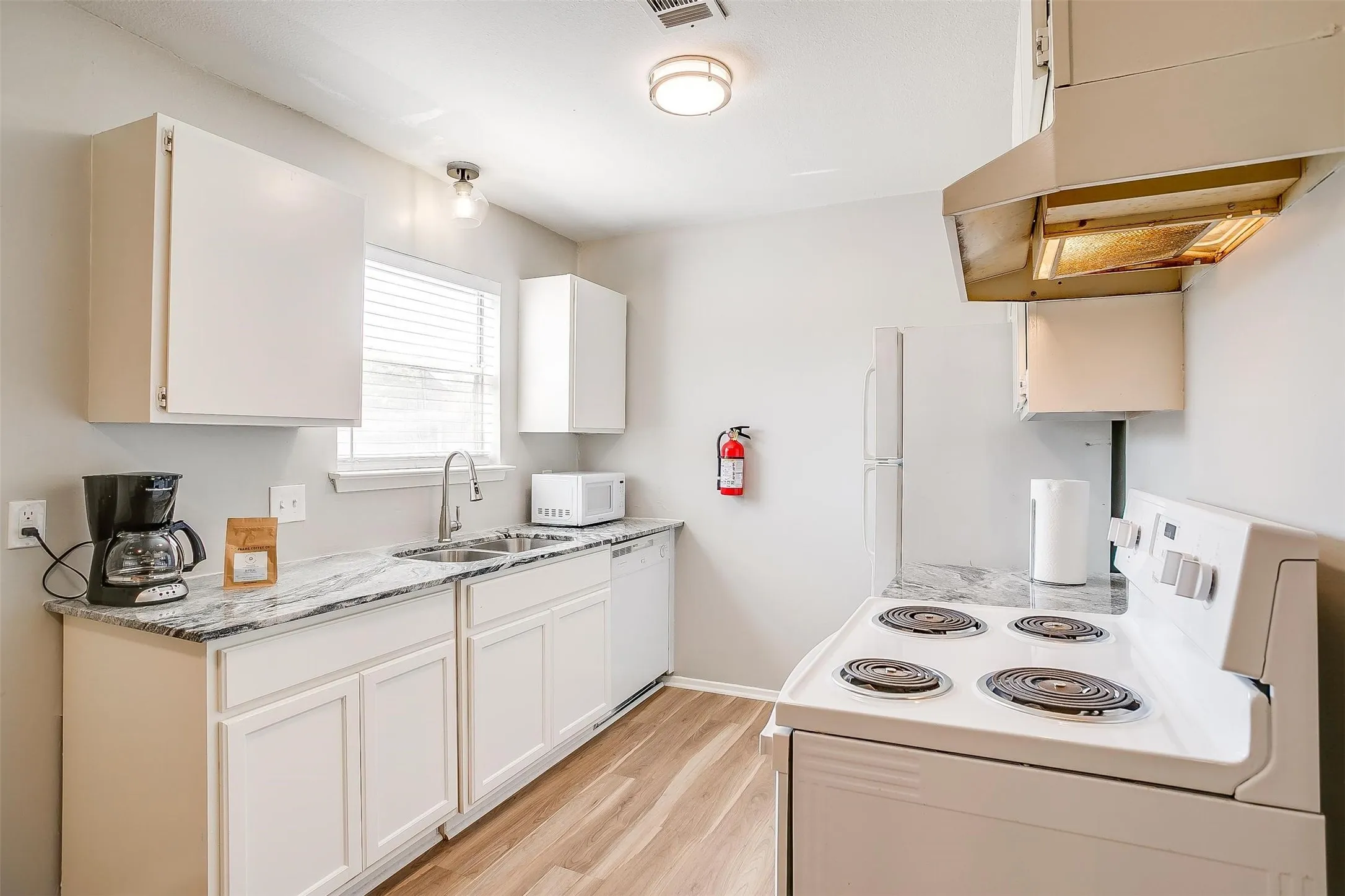 Kitchen featuring white cabinetry, light-toned wood-finish flooring, a double basin sink, and a white electric range with an overhead exhaust hood