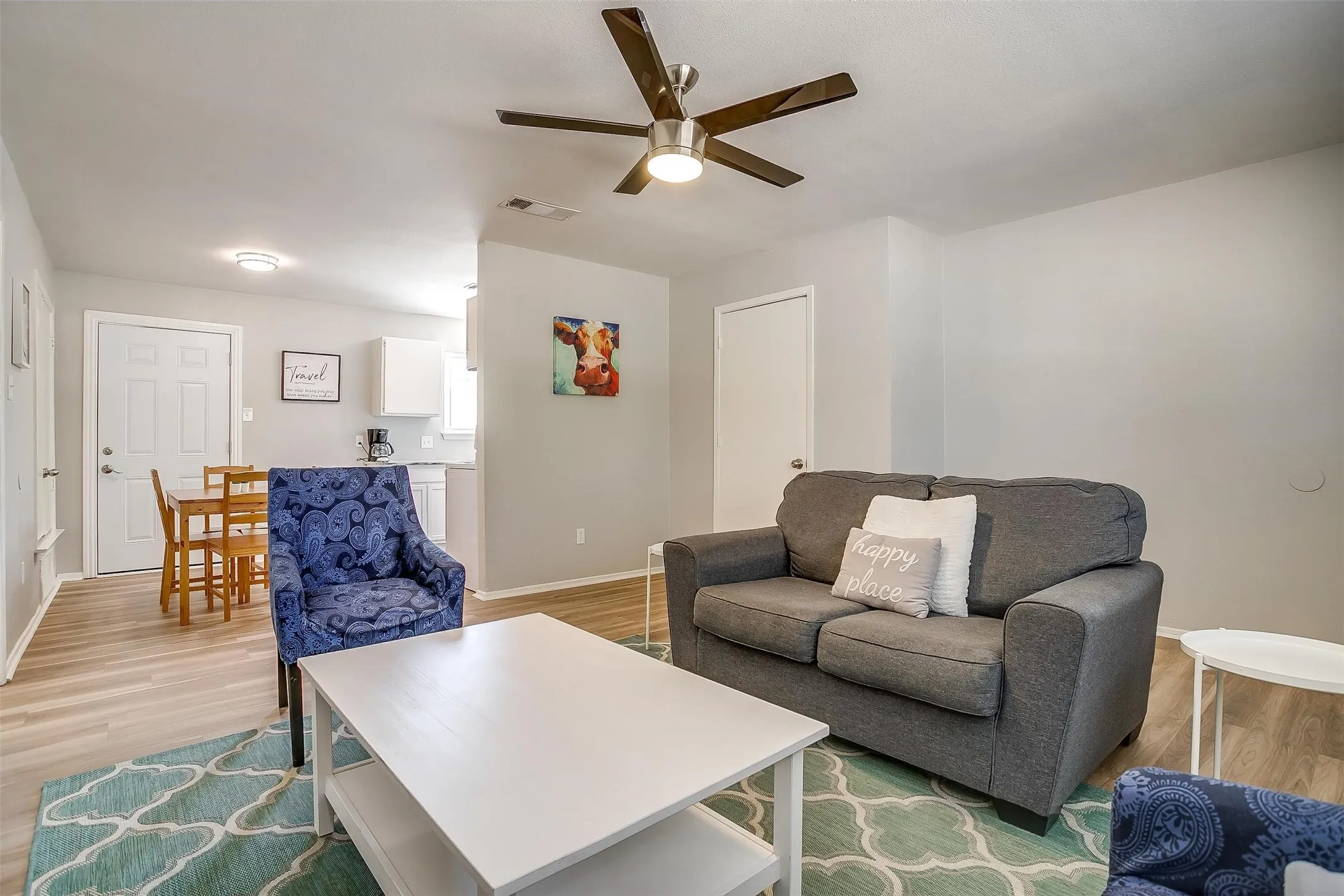 Open-concept living space featuring wood-finish flooring, a ceiling fan with integrated lighting, and light gray wall tones