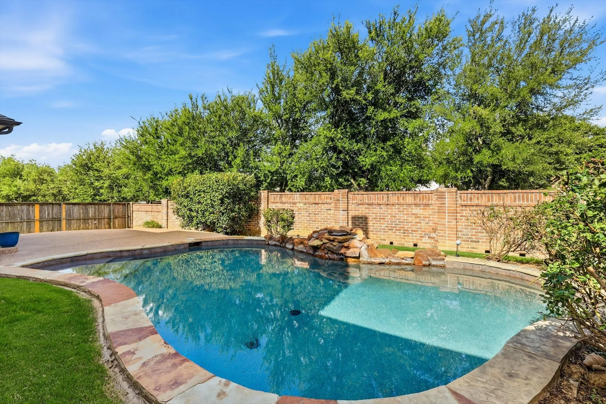 Swimming pool with a stone waterfall feature, concrete decking, stone coping, and a brick privacy wall