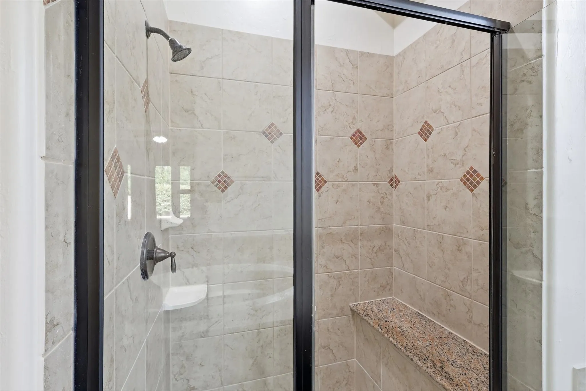 Tiled shower enclosure with a dark bronze showerhead, built-in soap dish, and a granite-topped shower bench