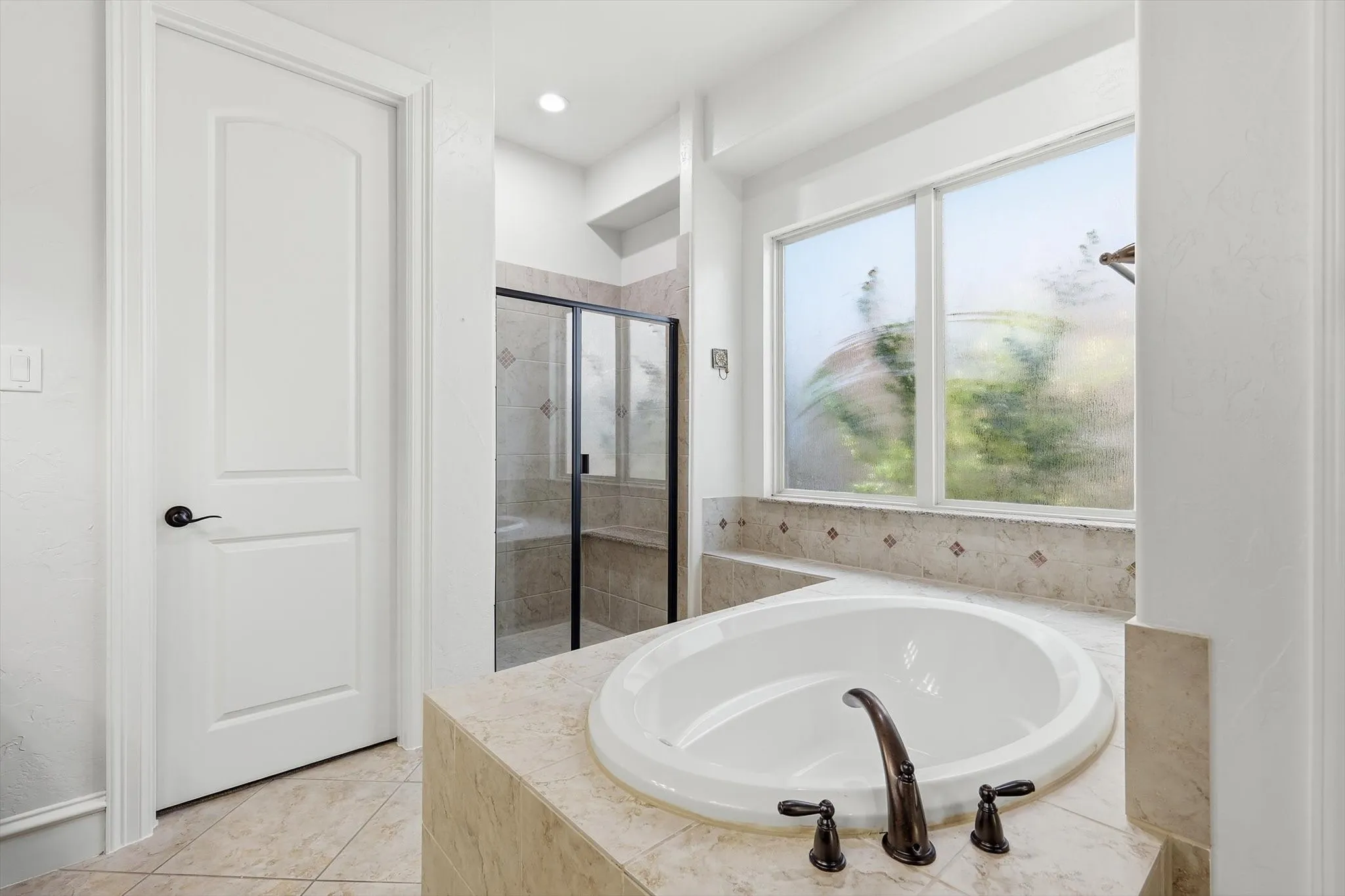 Built-in soaking tub with dark bronze fixtures, tile surround, and an adjacent multi-pane window