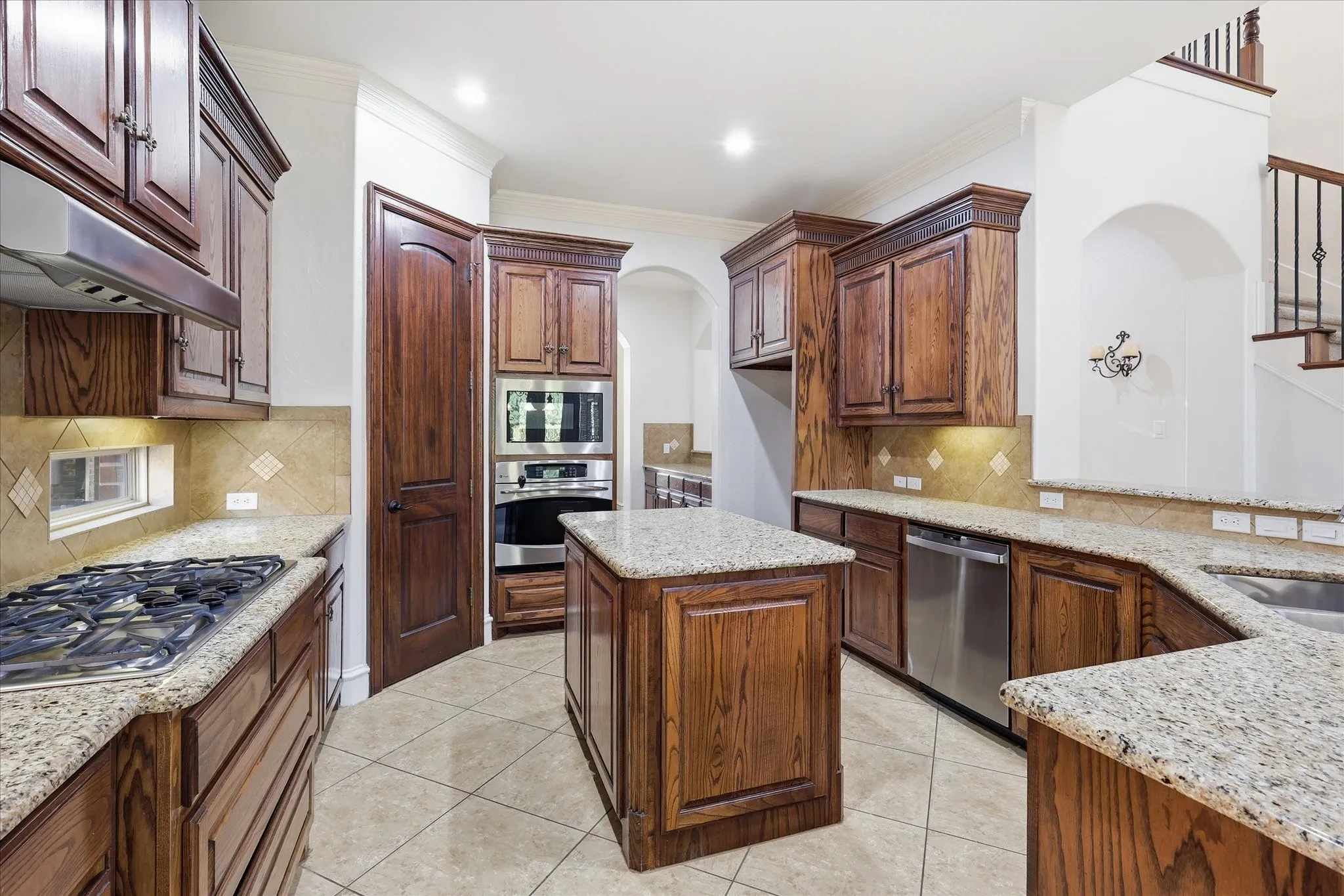 Kitchen featuring wood cabinetry, light-toned stone countertops, built-in stainless steel appliances, and tile flooring