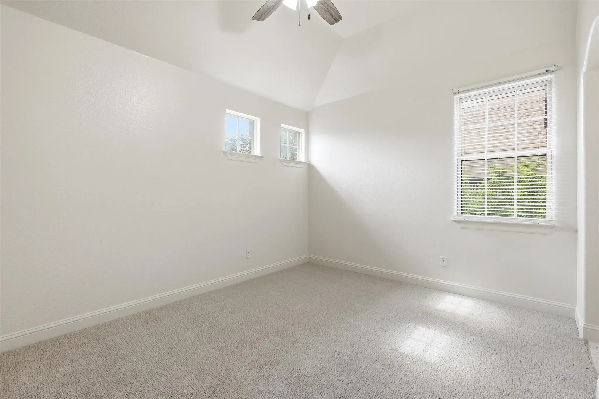 Vaulted ceiling, ceiling fan, multiple windows, window blinds, and light-colored carpeting