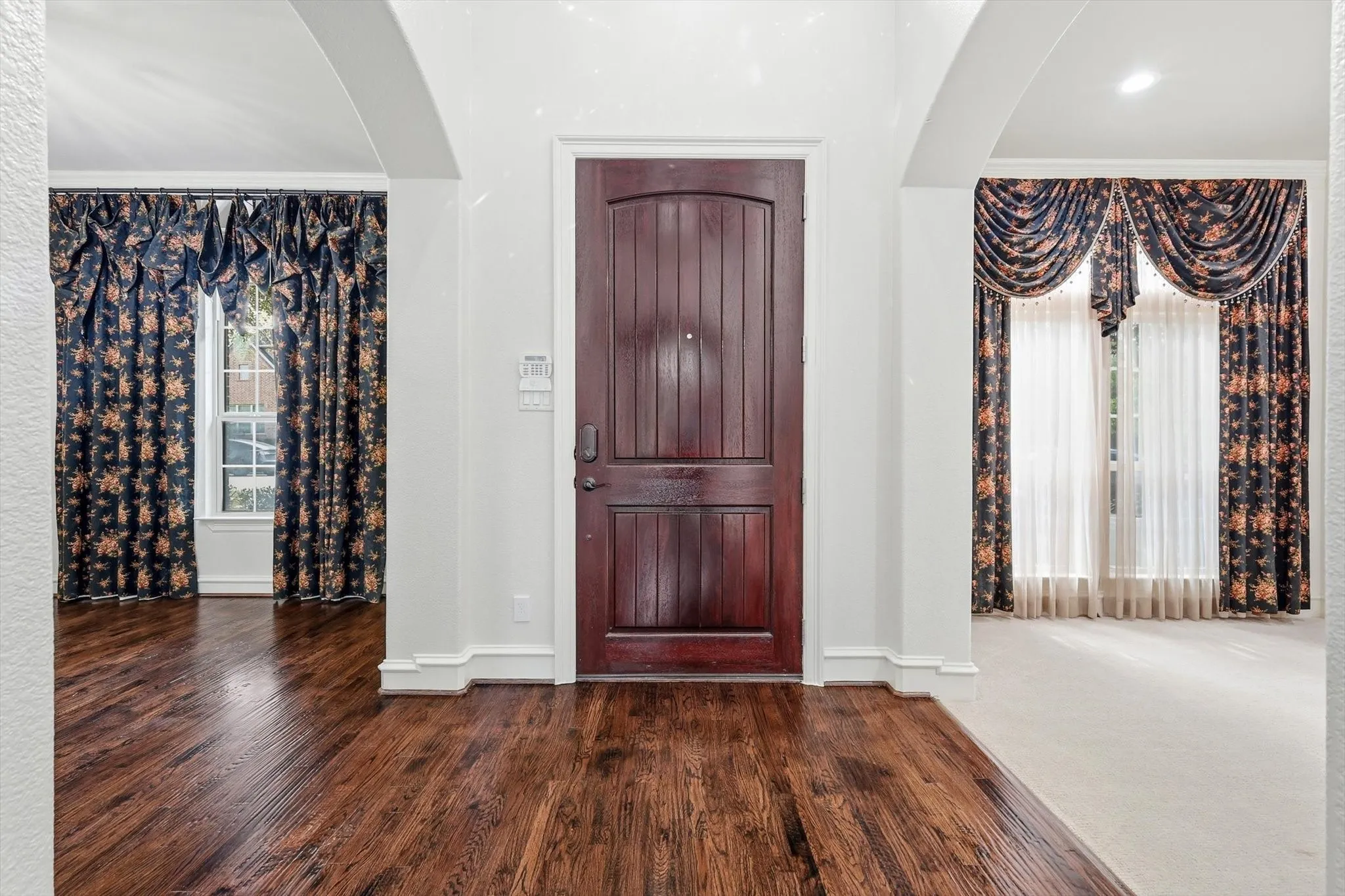 Rich wood-paneled entry door, arched doorways, hardwood flooring, and recessed lighting