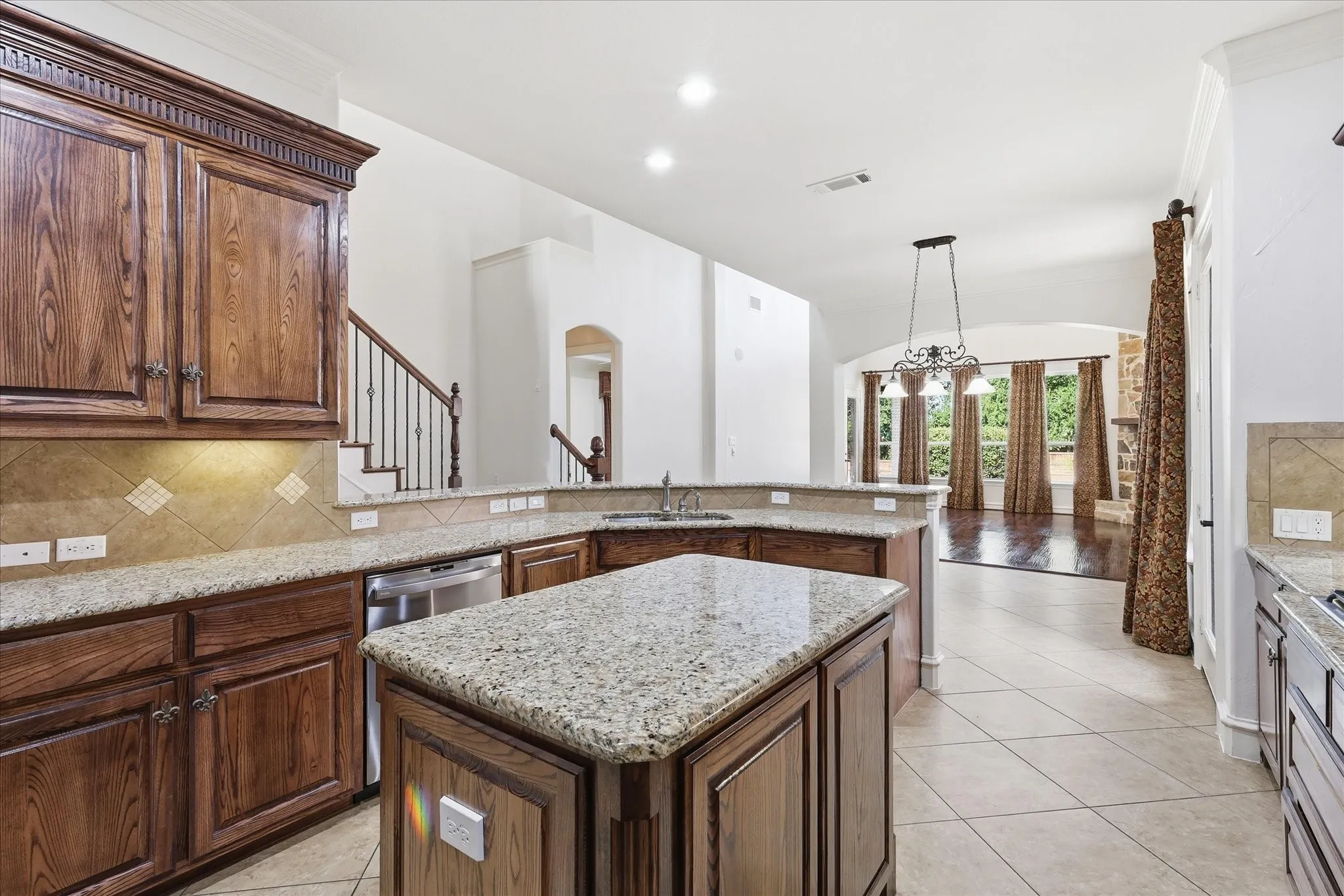 Open-concept kitchen with granite countertops, wood cabinetry, tile backsplash, and stainless steel appliances