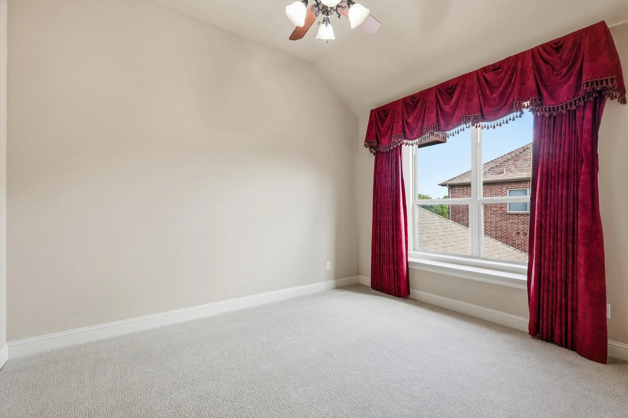 Vaulted ceiling with a ceiling fan, carpeted flooring, and a large window