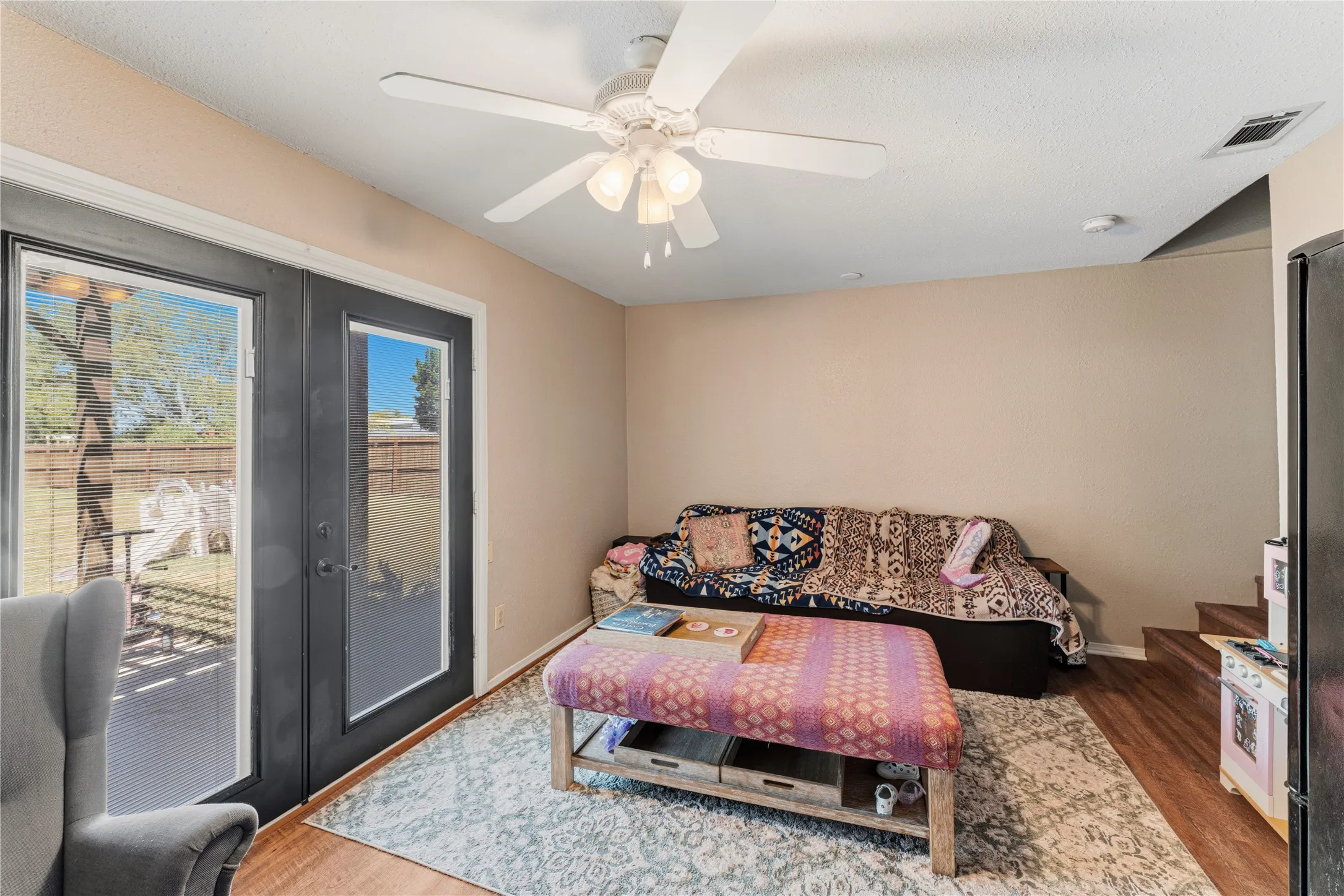 French doors opening to an outdoor patio, wood-finish flooring, ceiling fan with integrated lighting, and neutral wall tones