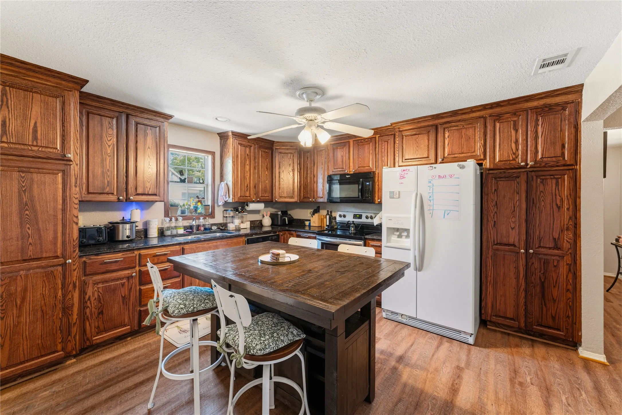 Wood-finish flooring, dark wood cabinetry, black countertops, and a central island with seating