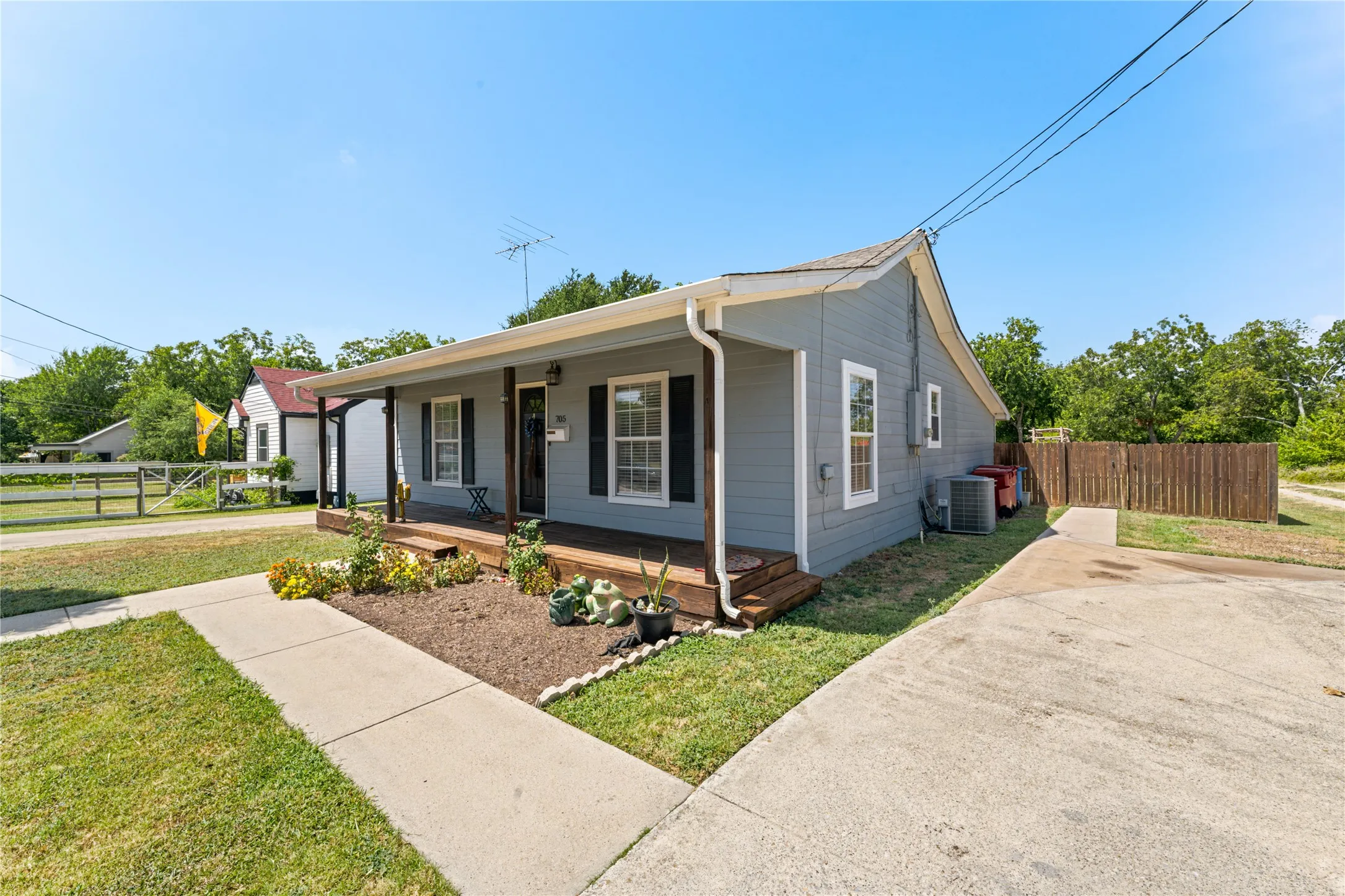 Gray exterior siding with white trim, wood-finish porch, concrete walkway, and a concrete driveway