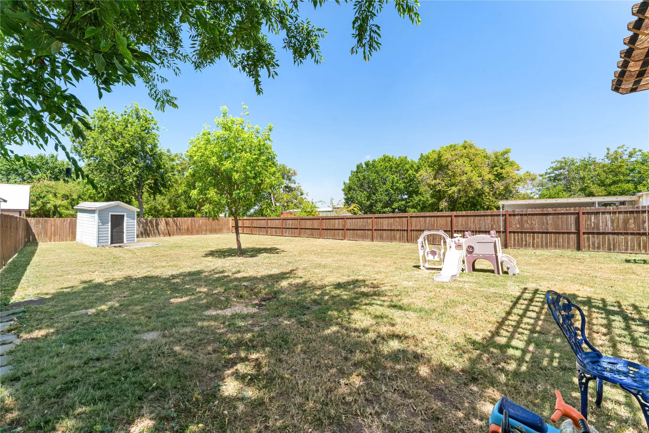 Expansive backyard with a full privacy fence, mature trees, and a storage shed