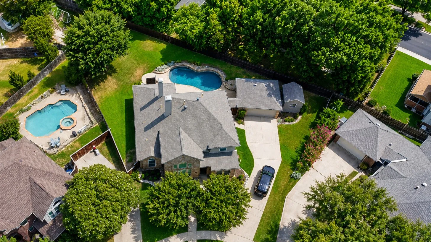 Expansive backyard featuring a freeform swimming pool, generous paved deck, mature privacy landscaping, and a detached structure
