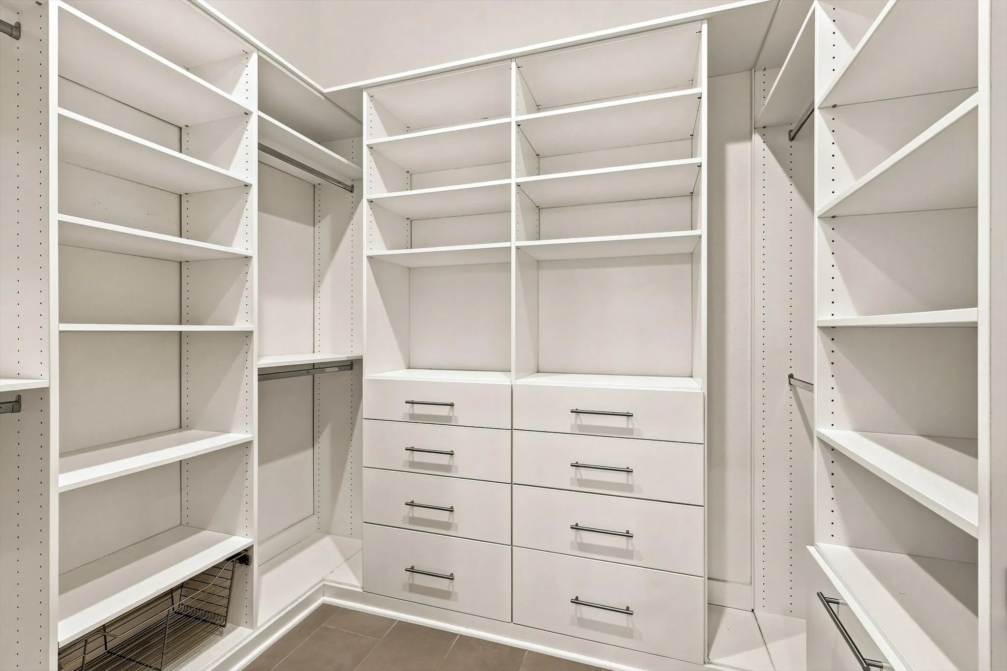 Custom closet system featuring extensive shelving, built-in drawers with modern pulls, garment hanging rods, and an integrated wire basket