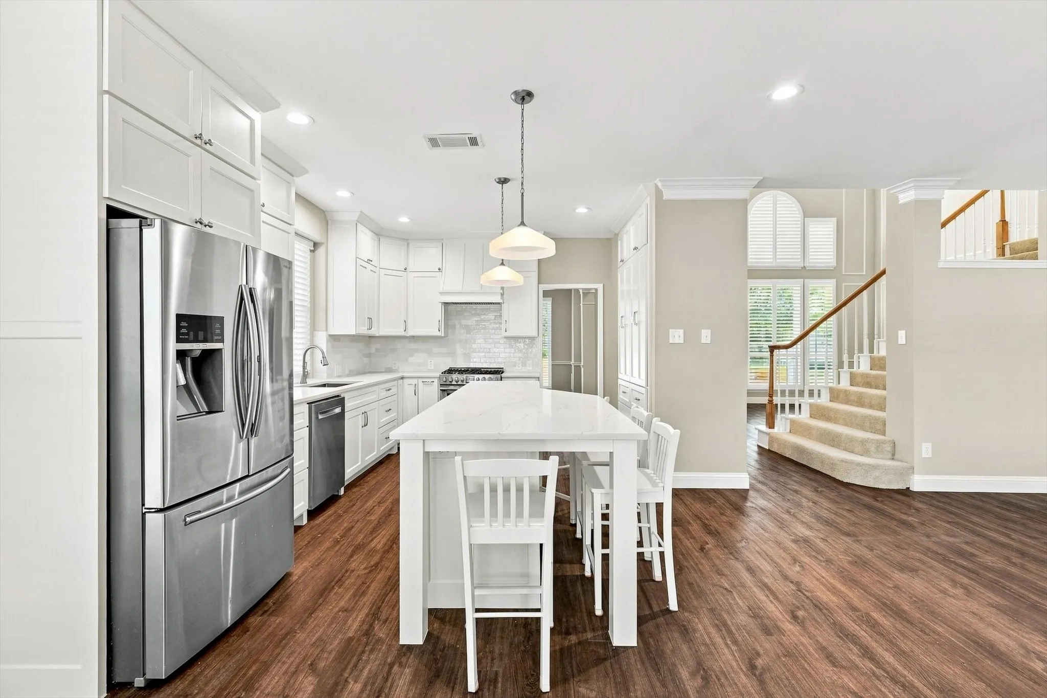 Contemporary kitchen featuring white cabinetry, stainless steel appliances, a center island with pendant lighting, and wood-finish flooring