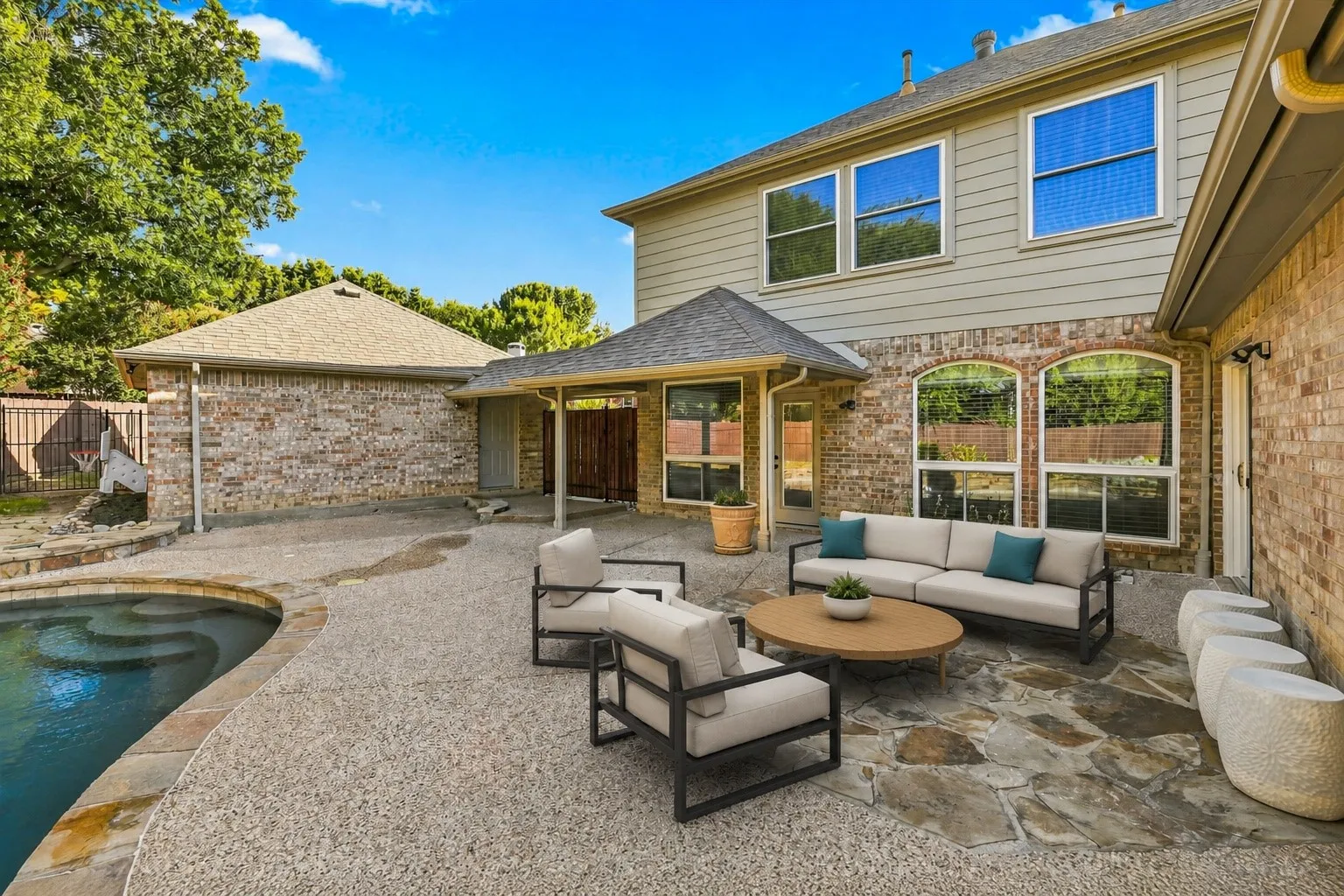Expansive outdoor space featuring a swimming pool, stone coping, and an exposed aggregate patio