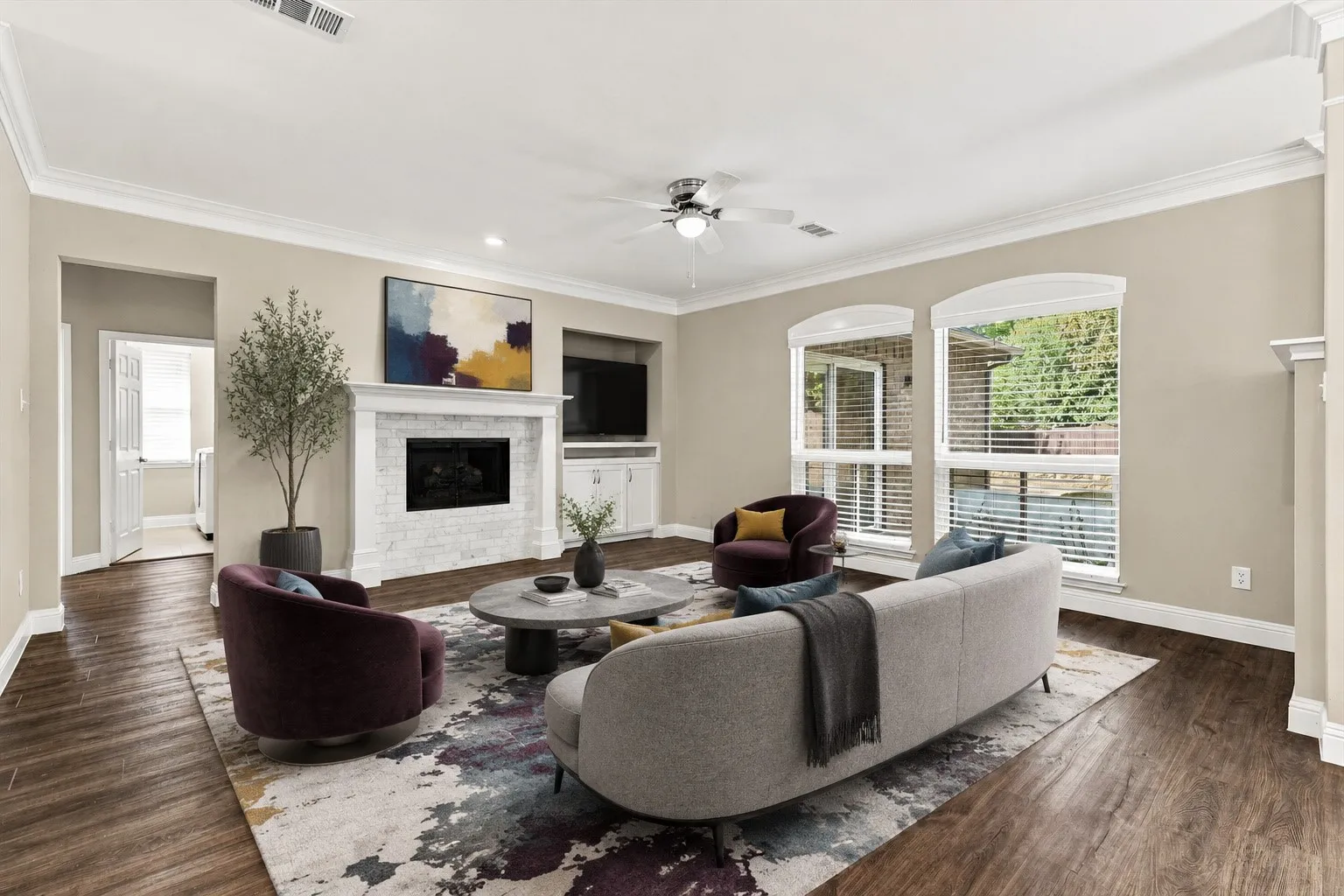 Virtually Staged Living area featuring wood flooring, a white-tiled fireplace with a mantel, built-in cabinetry, arched windows, and crown molding
