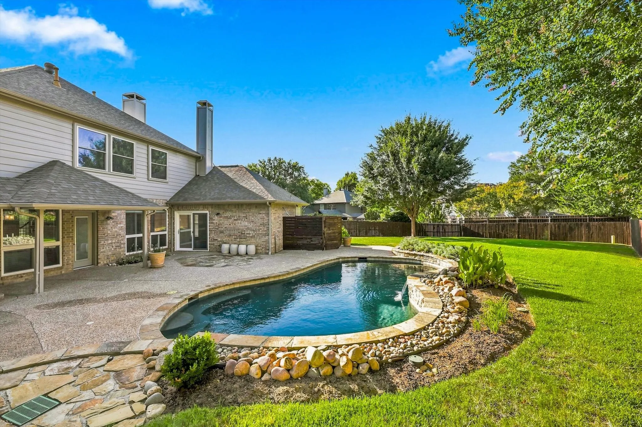 In-ground pool with stone coping, expansive patio, lush lawn, and privacy fencing