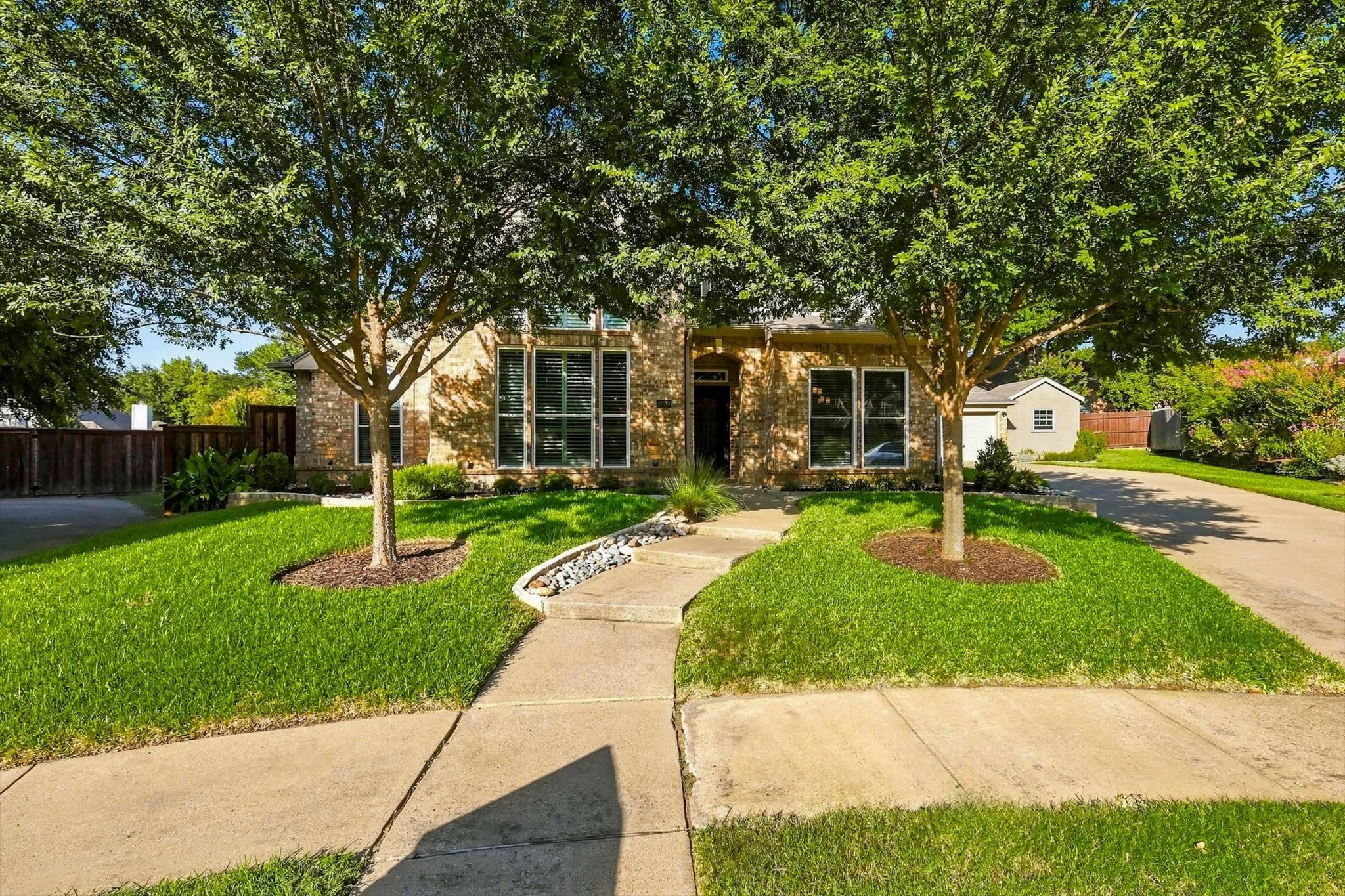 Brick facade with a concrete walkway, and a landscaped front yard with mature trees