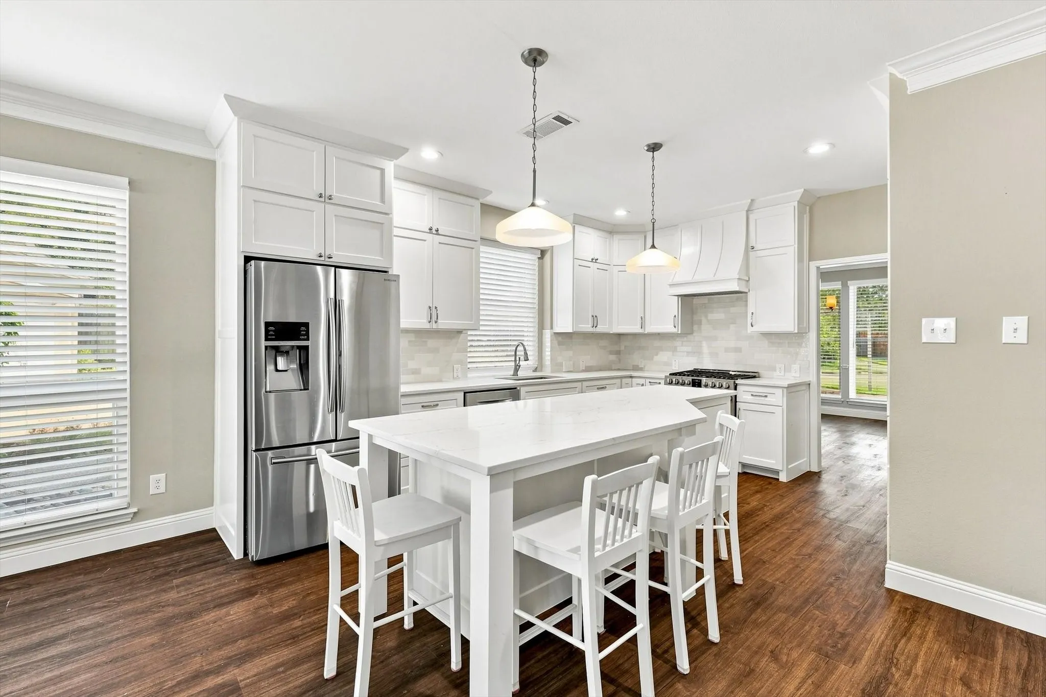 Kitchen featuring white cabinetry, stainless steel appliances, a center island with countertop seating, wood-finish flooring, and pendant lighting