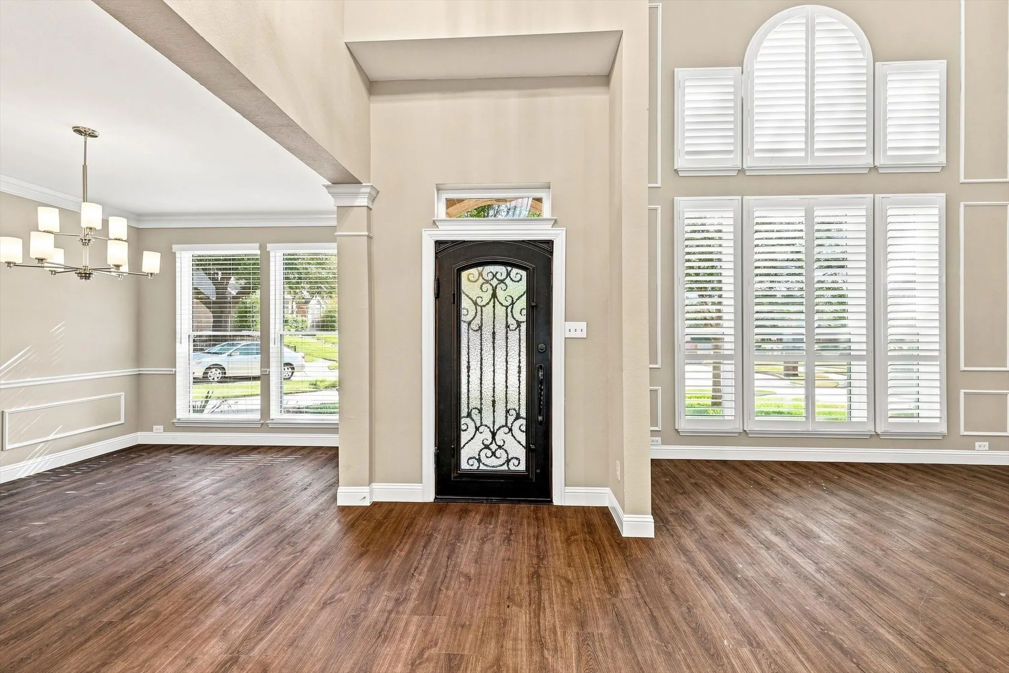 Two-story entry with wood-finish flooring, an ornate wrought iron front door, and a multi-pane window with arched transom
