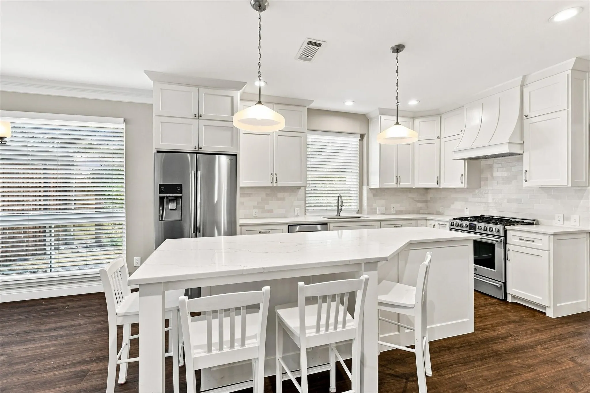 Spacious kitchen featuring an expansive island, stainless steel appliances, white cabinetry, a tiled backsplash, and wood-finish flooring