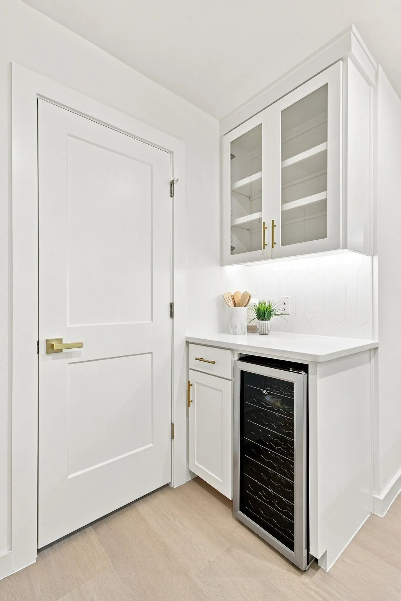 Built-in beverage refrigerator, white cabinetry with glass inserts, under-cabinet lighting, and light wood-finish flooring