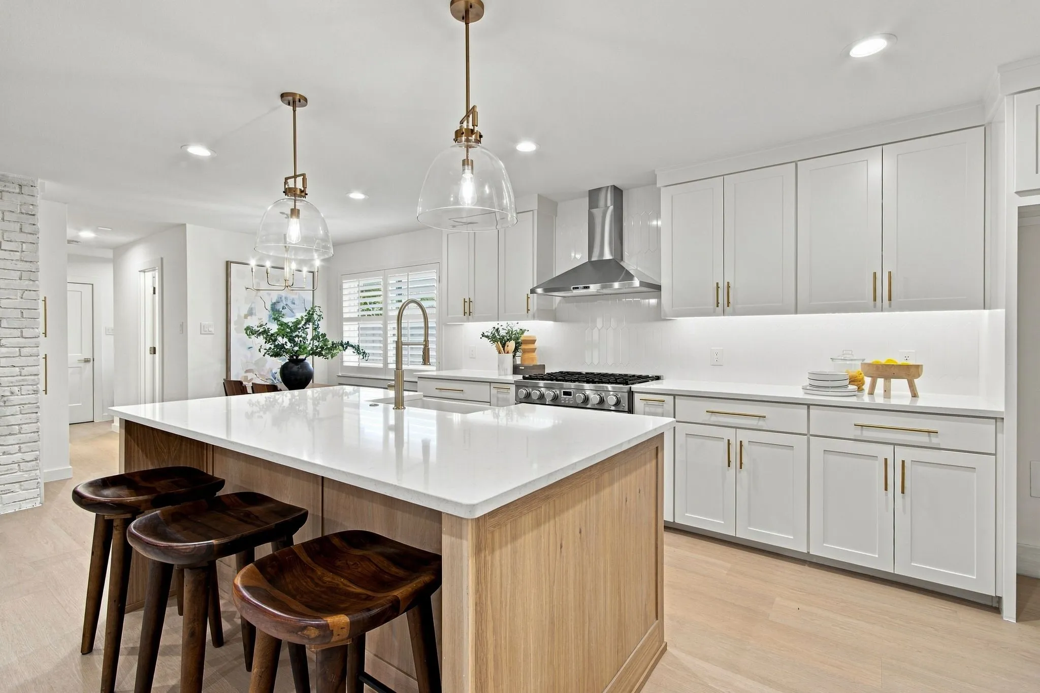 Kitchen featuring a center island with a stone countertop, white shaker cabinetry with gold-tone hardware, a stainless steel range hood, and wood-finish flooring