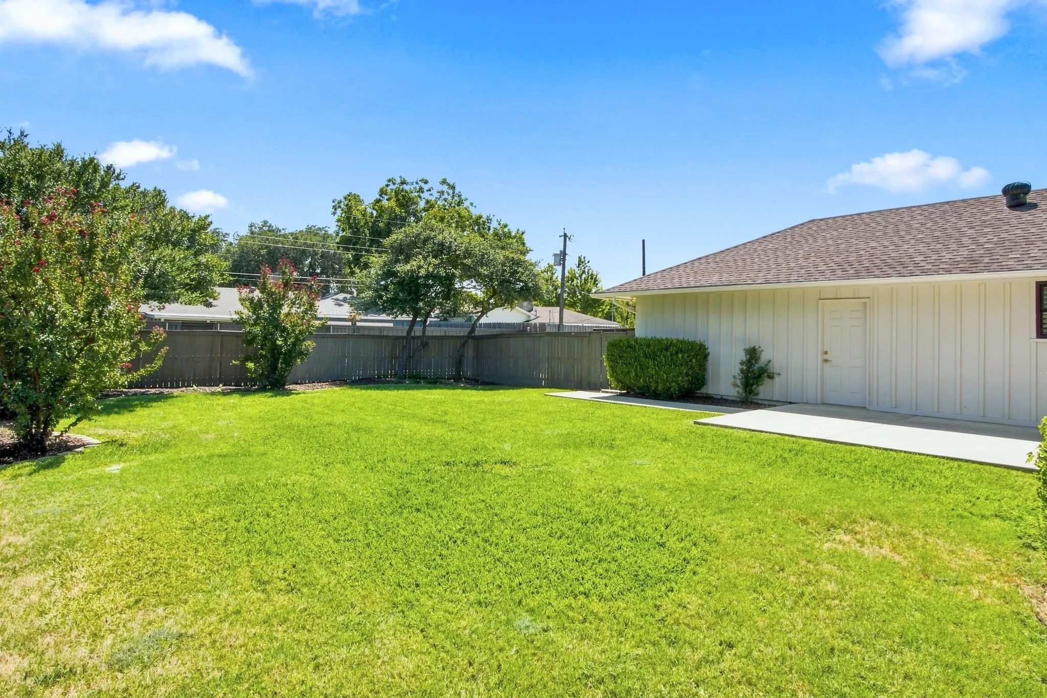 Expansive backyard with a lush lawn, privacy fencing, mature trees, and a concrete patio