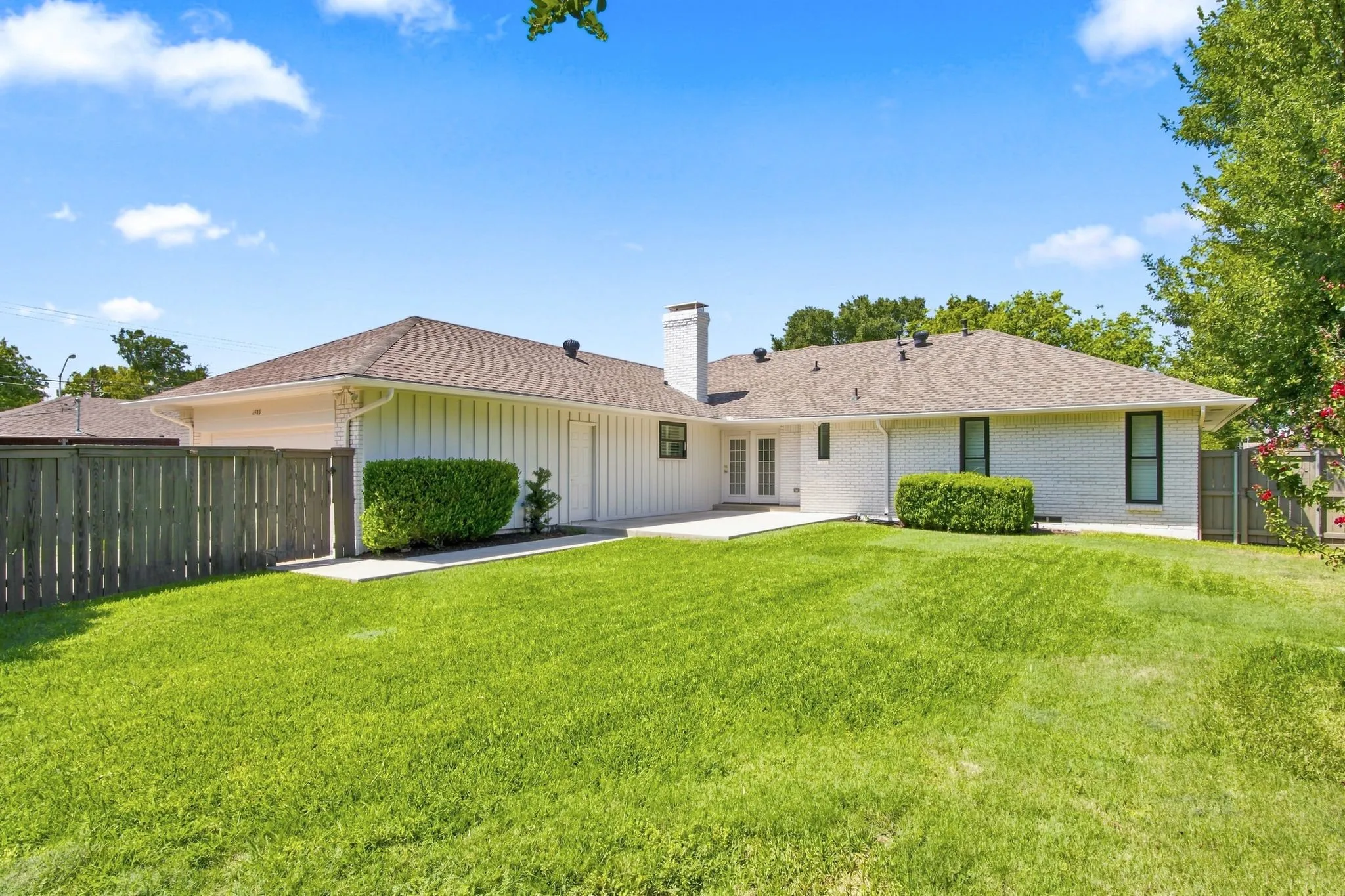 Expansive green lawn with a white brick exterior, light brown shingle roof, and a privacy fence