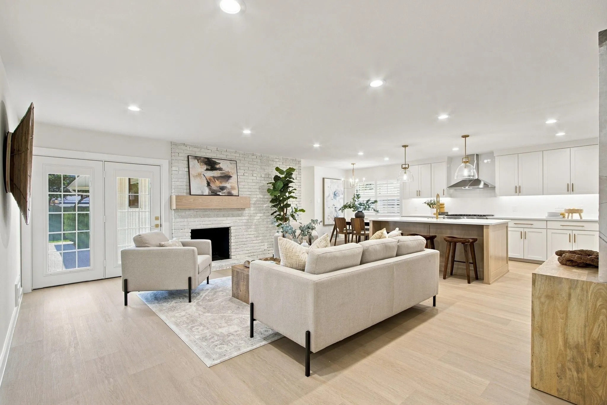 Open-concept living space featuring brick wood burning fireplace with a wood mantle, recessed lighting, and french door to patio