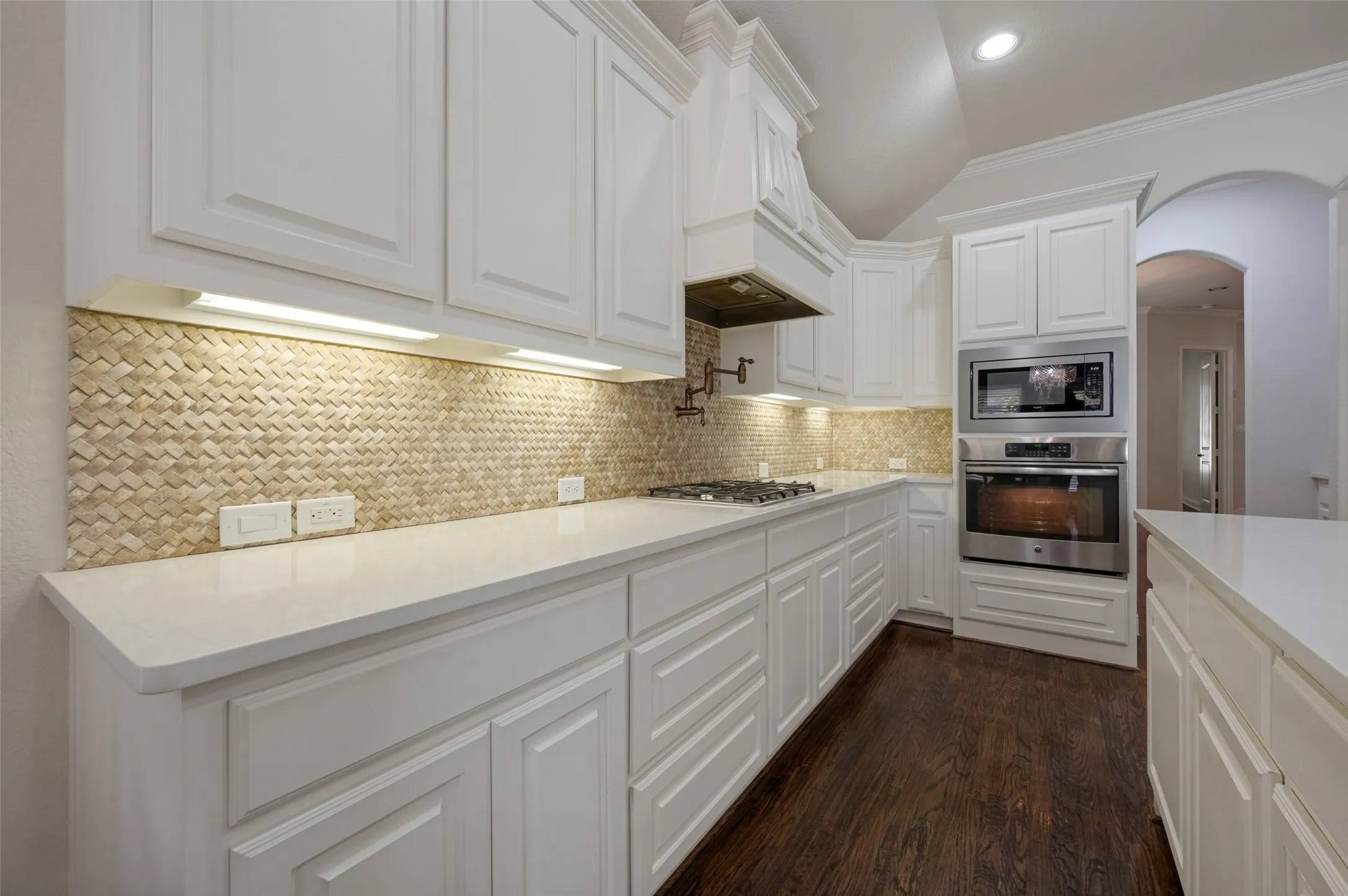 White cabinetry, light-toned countertops, tile backsplash, wood-finish flooring, and stainless steel built-in appliances