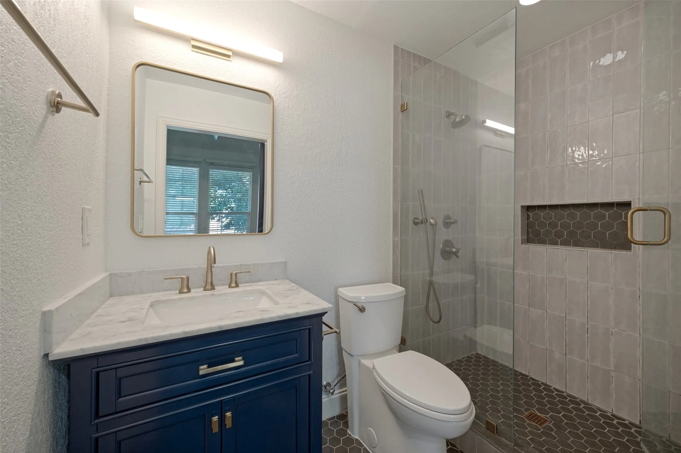 Vanity with white countertop and integrated sink, framed mirror, glass-enclosed shower, wall-mounted shower system, and tiled shower niche