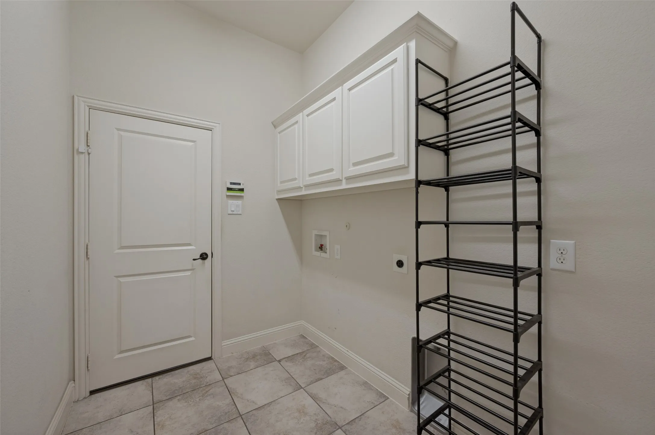 White shaker-style cabinetry with crown molding, tiled flooring, and a two-panel interior door with matte black hardware