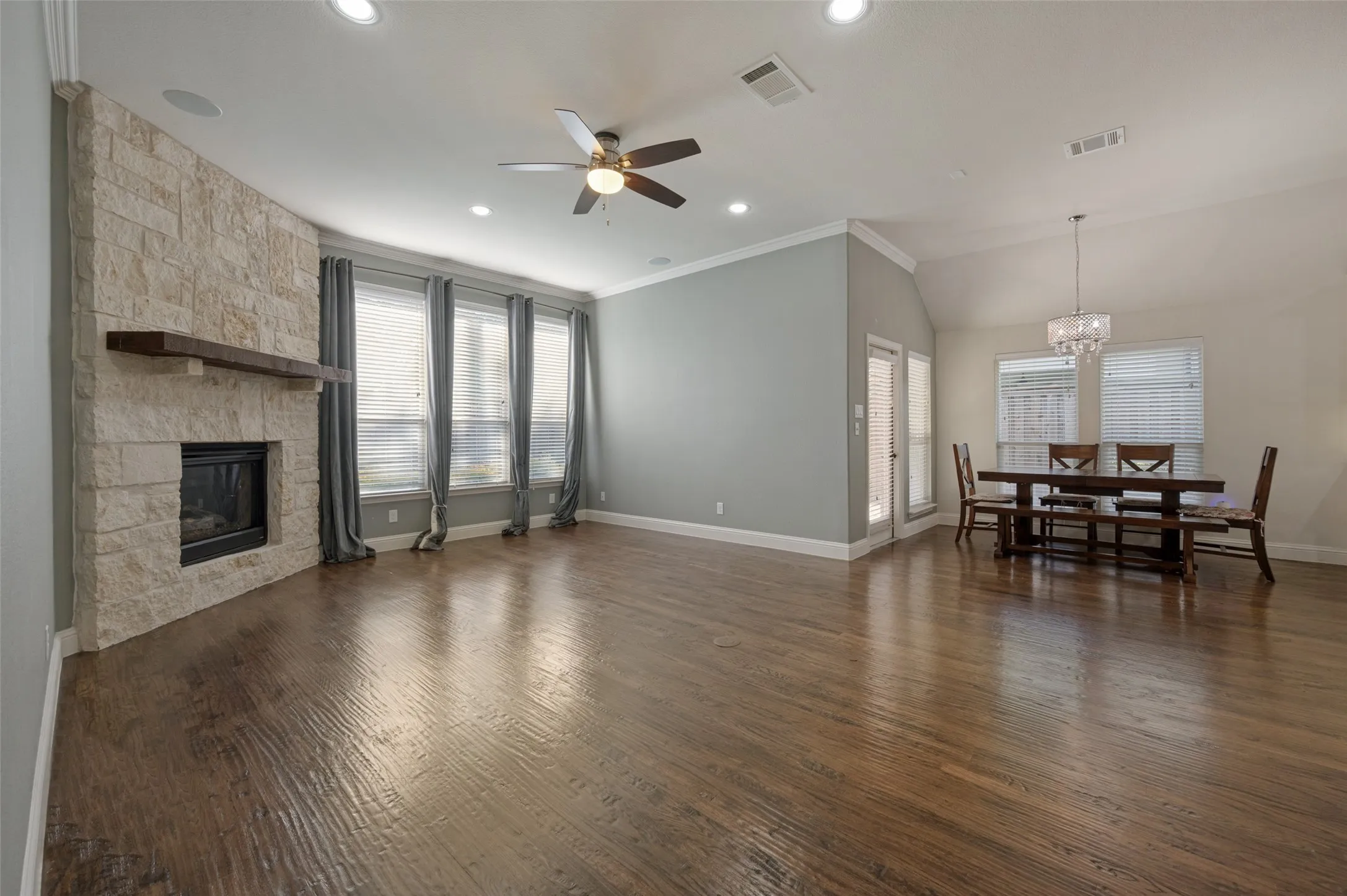 Open concept living space featuring wood-finish flooring, a stone-clad fireplace with a wood mantle, and recessed lighting