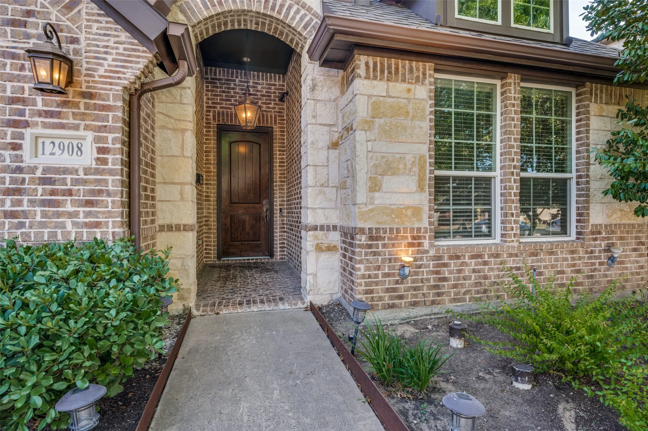 Brick and stone facade with an arched entryway, featuring a wood-panel door and a pendant light fixture