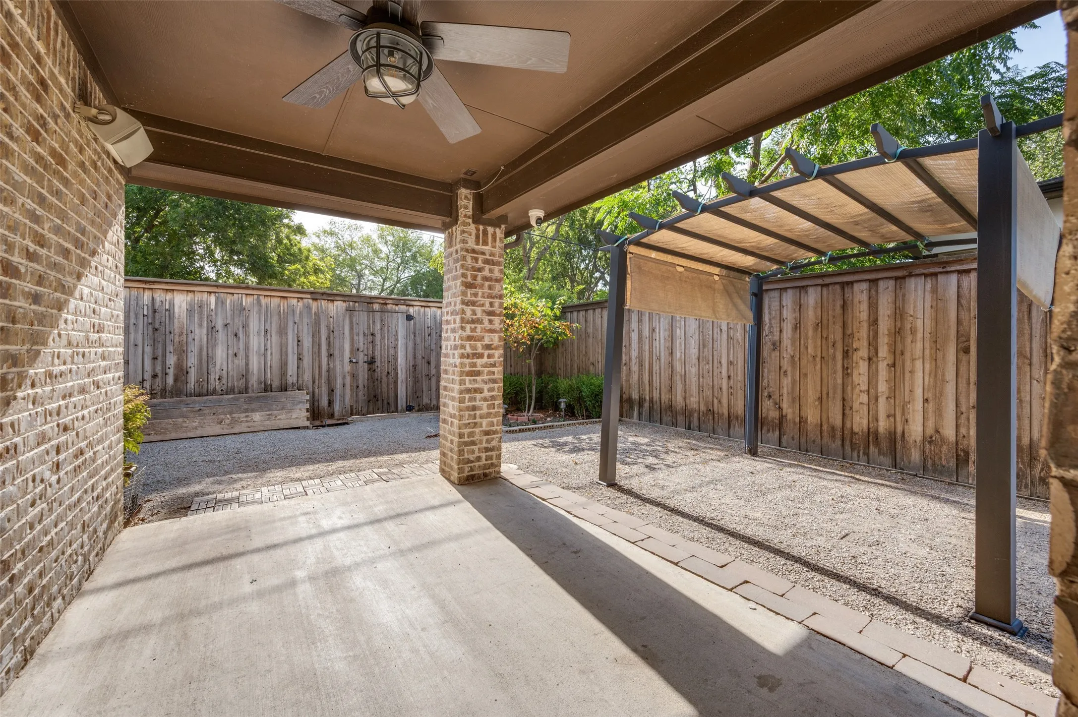 Covered patio with concrete flooring, brick columns, ceiling fan, and a separate pergola structure with a fabric canopy