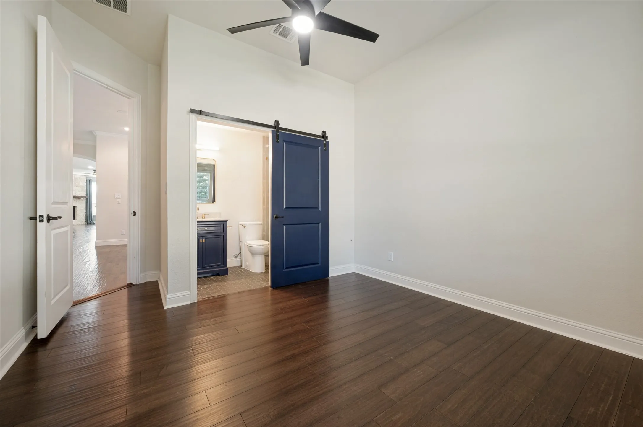 Dark wood-finish flooring, white walls, ceiling fan, and a blue barn door
