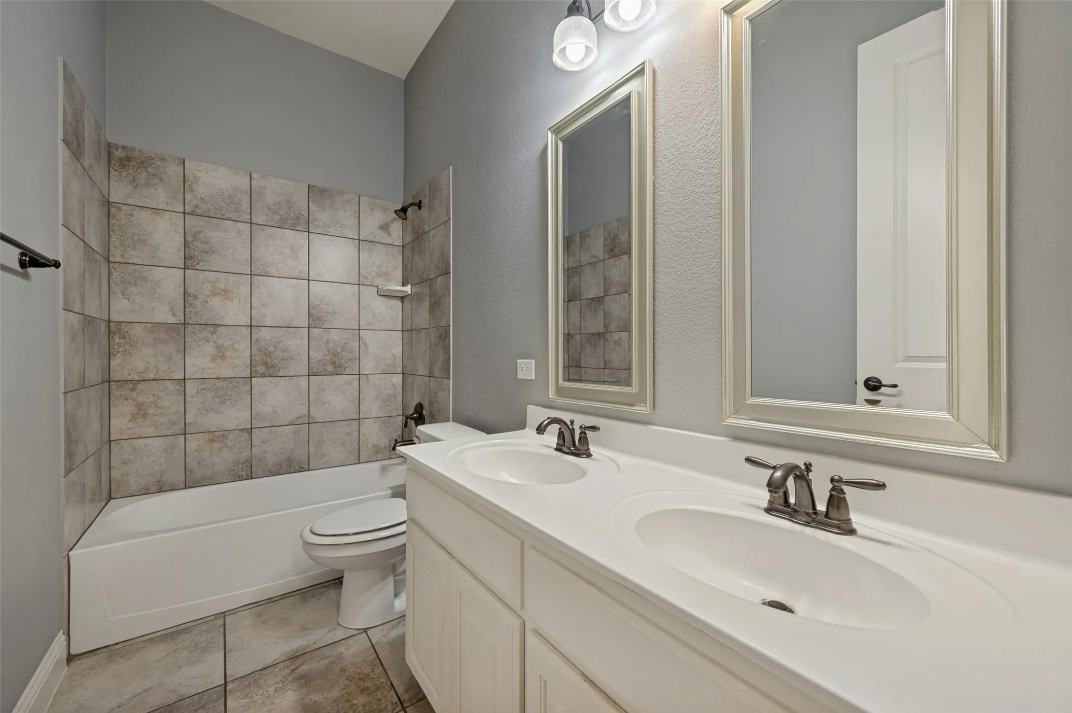 Bathroom featuring a double vanity with integrated sinks, framed mirrors, and a combination tub and shower with tile surround