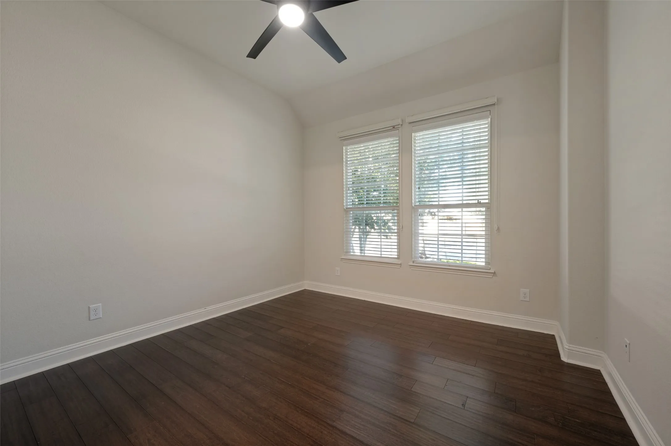 Wood-finish flooring, white wall paint, two windows with blinds, and an overhead ceiling fan