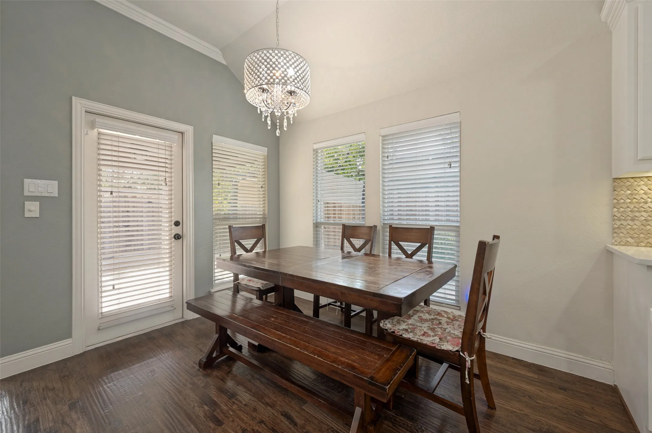 Vaulted ceiling with a crystal chandelier, wood-finish flooring, multiple windows, and a white paneled door