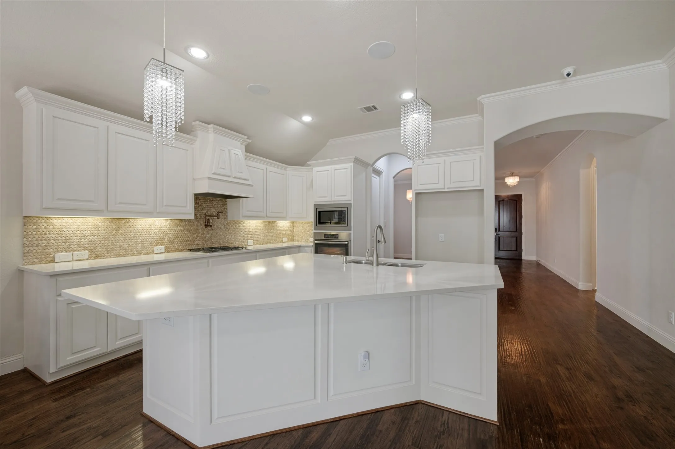 White cabinetry, large center island with integrated sink, patterned tile backsplash, dark wood-finish flooring, and recessed lighting