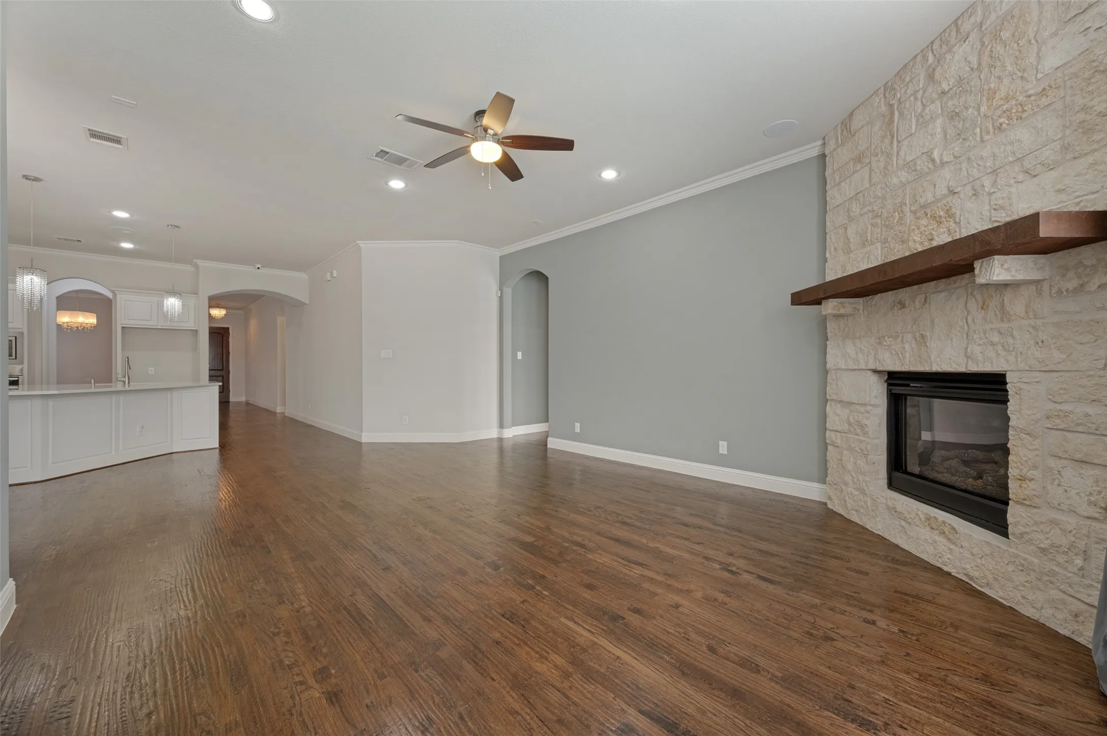 Spacious room featuring wood-finish flooring, a stone-clad fireplace with a wood mantle, recessed lighting, and a ceiling fan