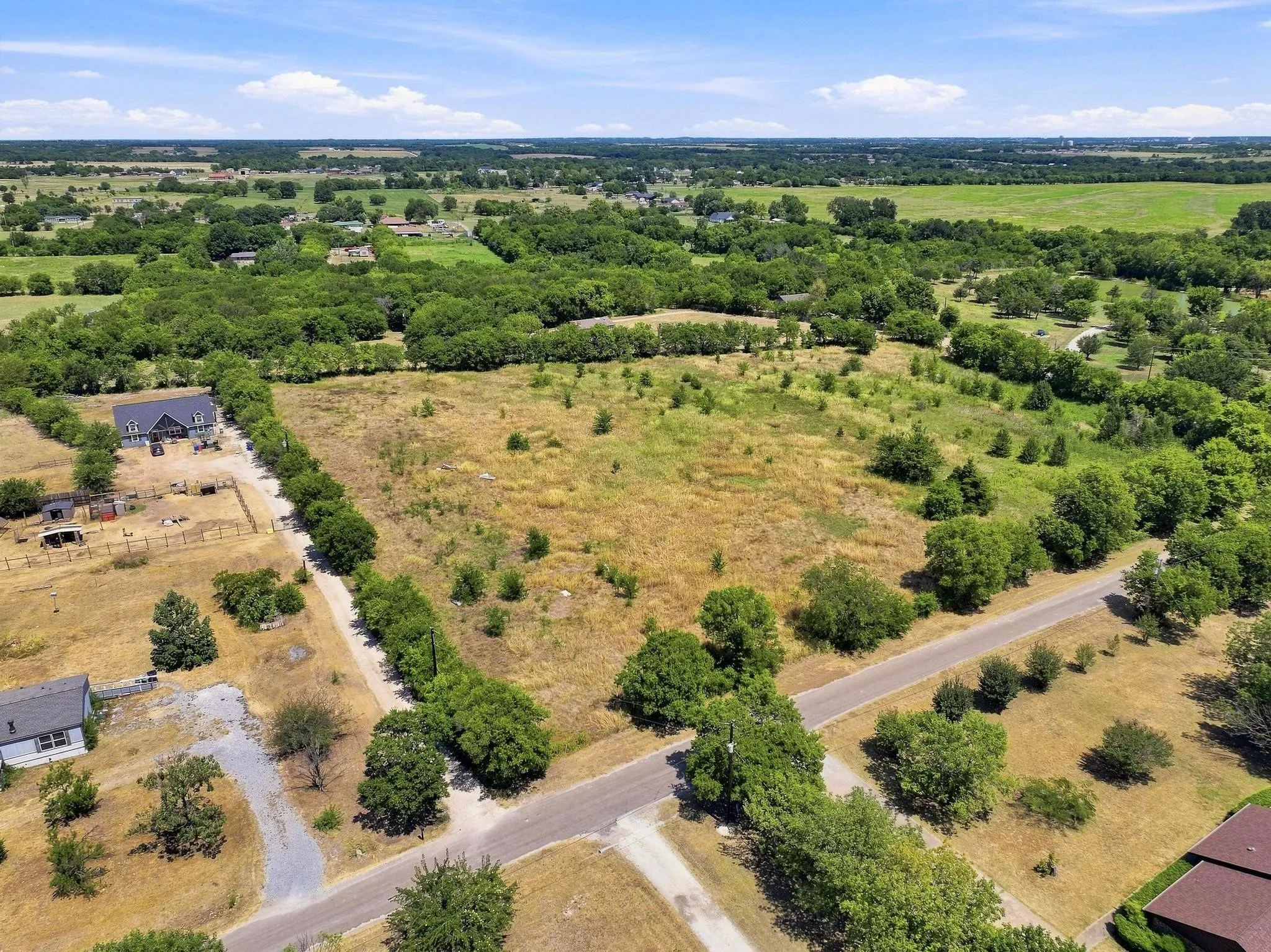 Expansive lot featuring mature trees, partial fencing, and paved road frontage
