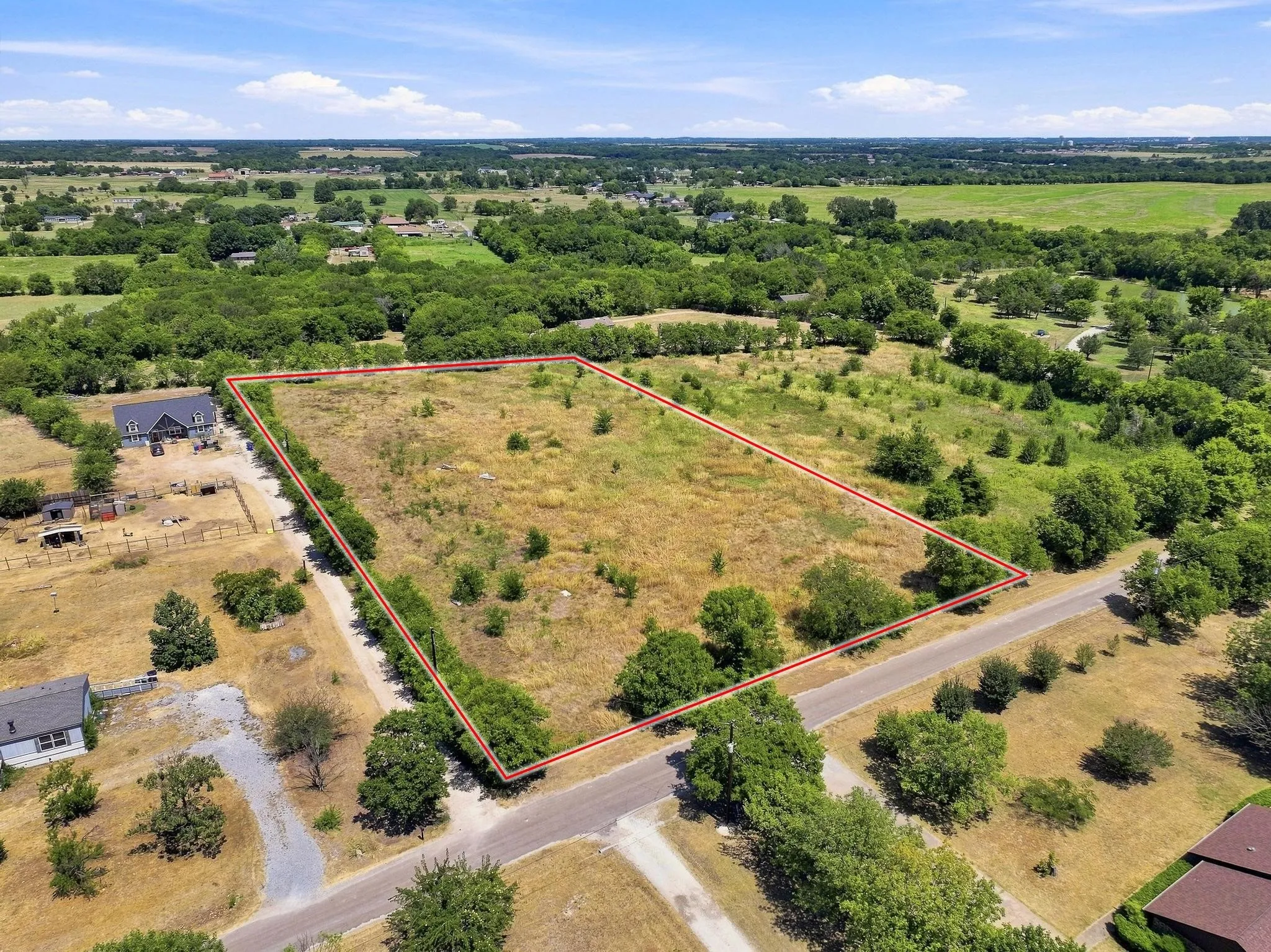 Expansive undeveloped land parcel featuring a clear boundary, direct road access, and scattered mature trees