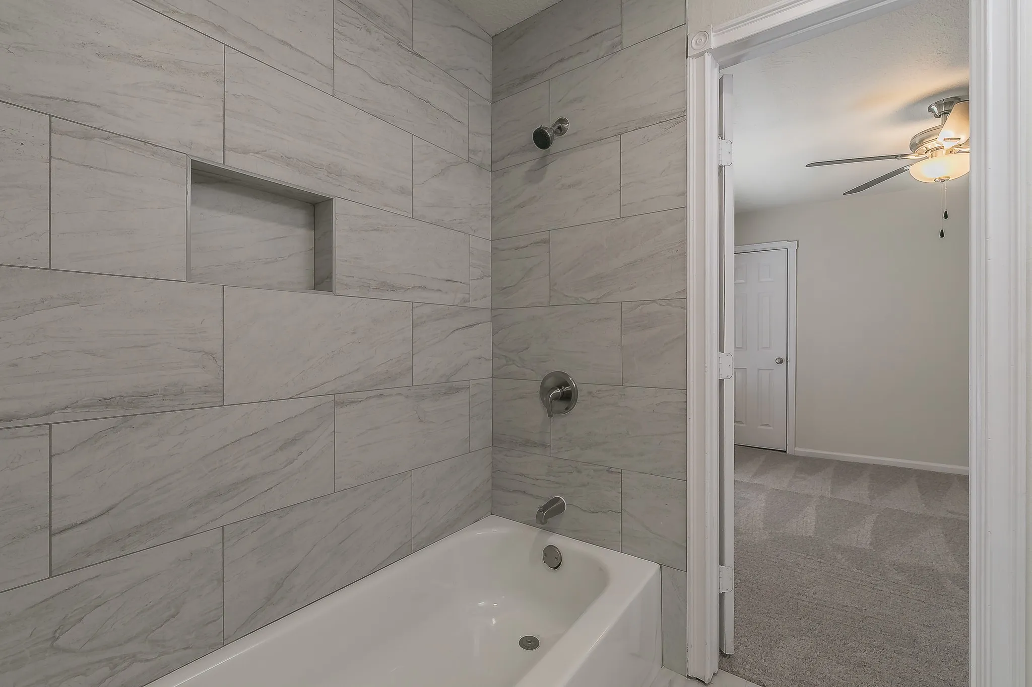 Bathtub with tiled surround, built-in shower niche, and brushed nickel fixtures